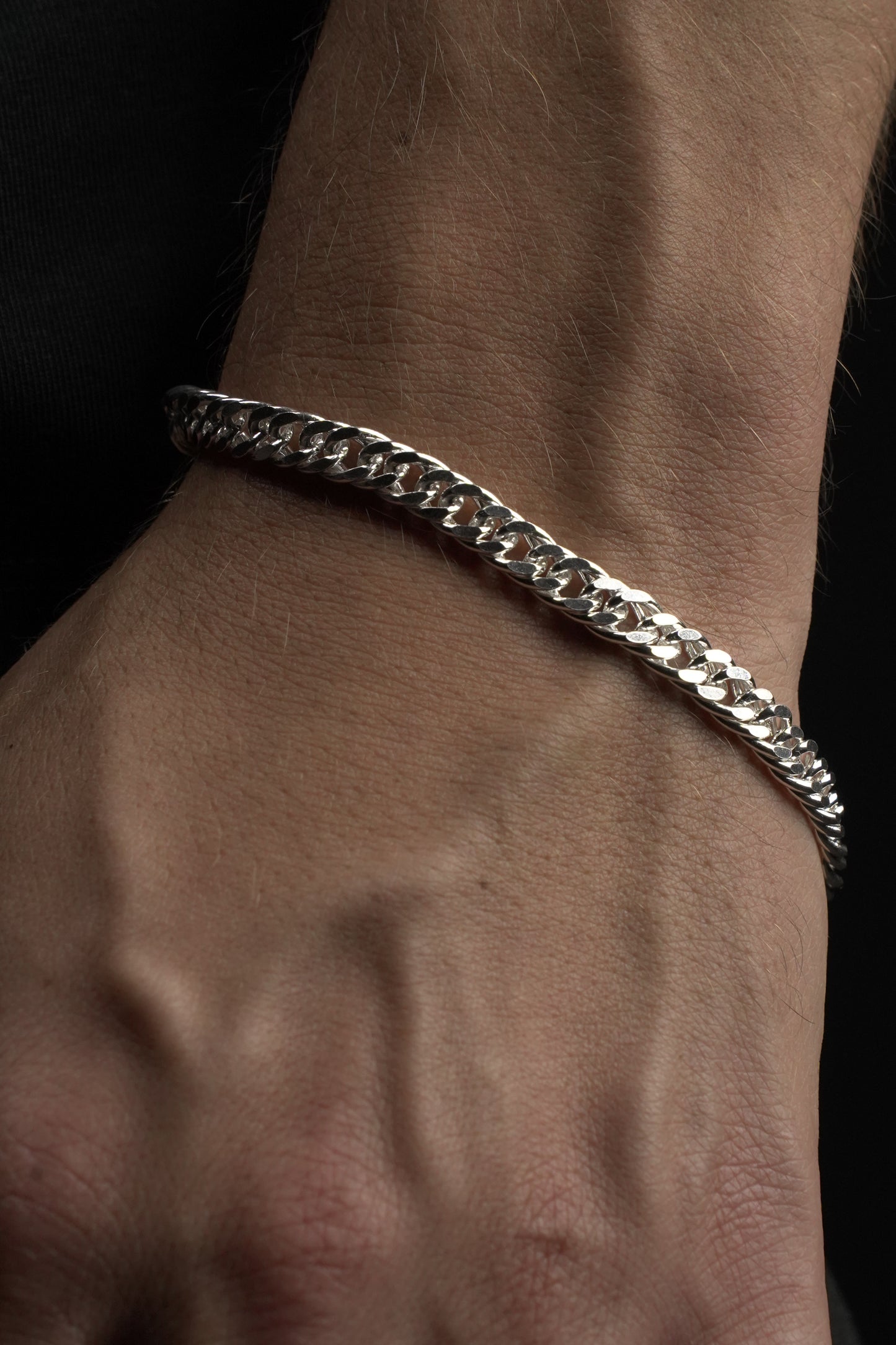 Silver chain bracelet on a wrist against a dark background