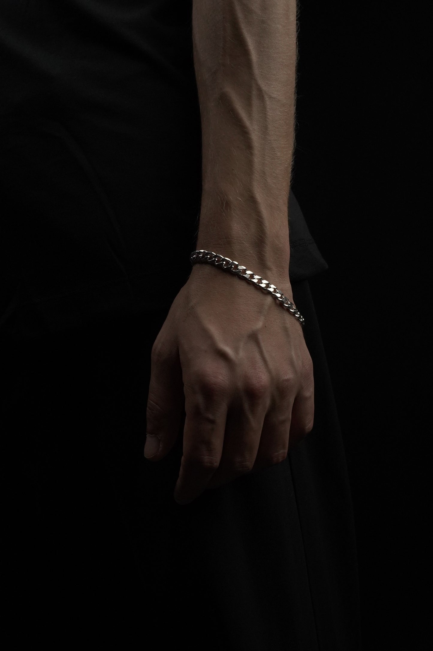 Hand wearing a silver chain bracelet on a dark background