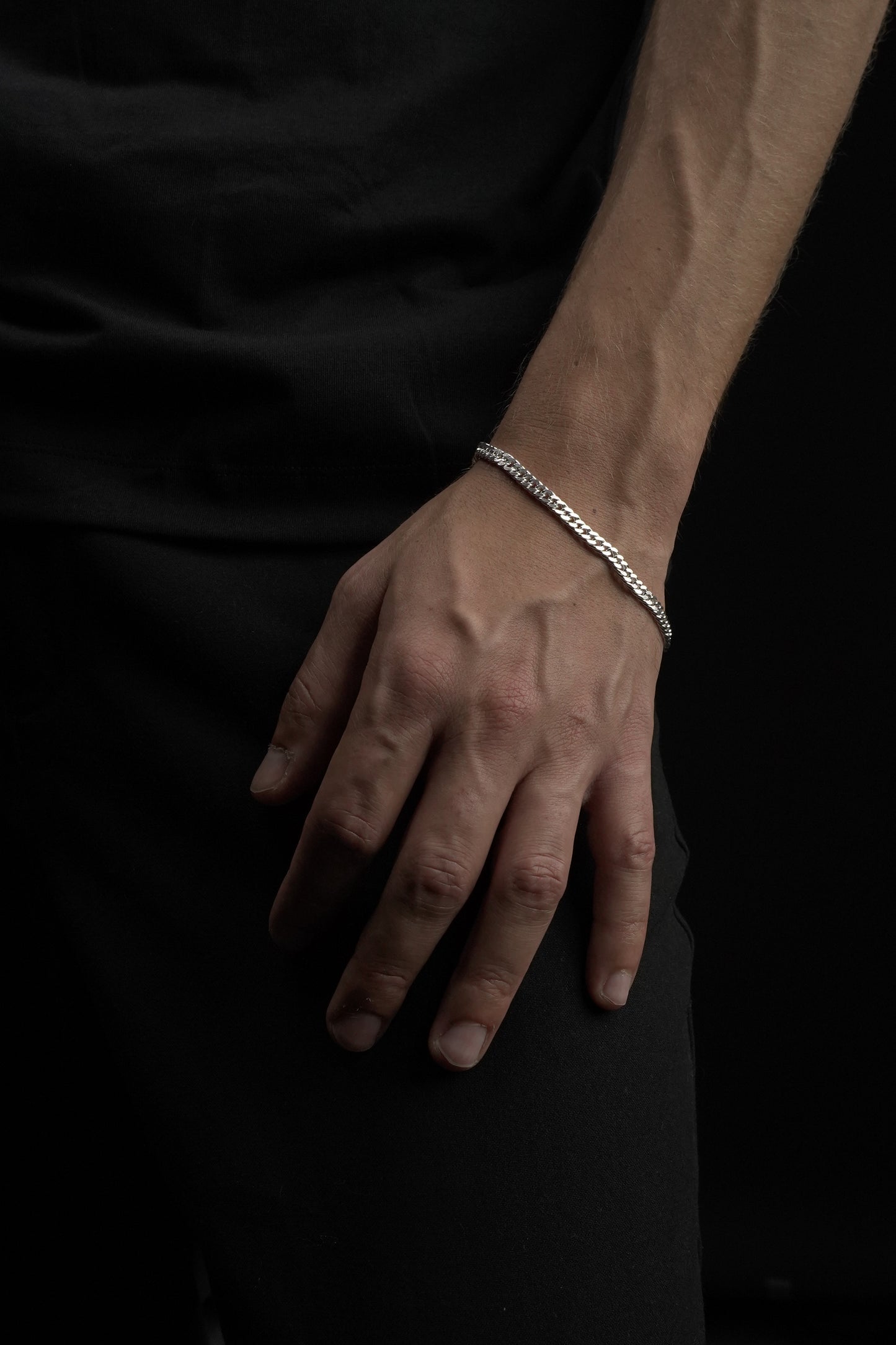 Hand wearing a silver bracelet on a dark background