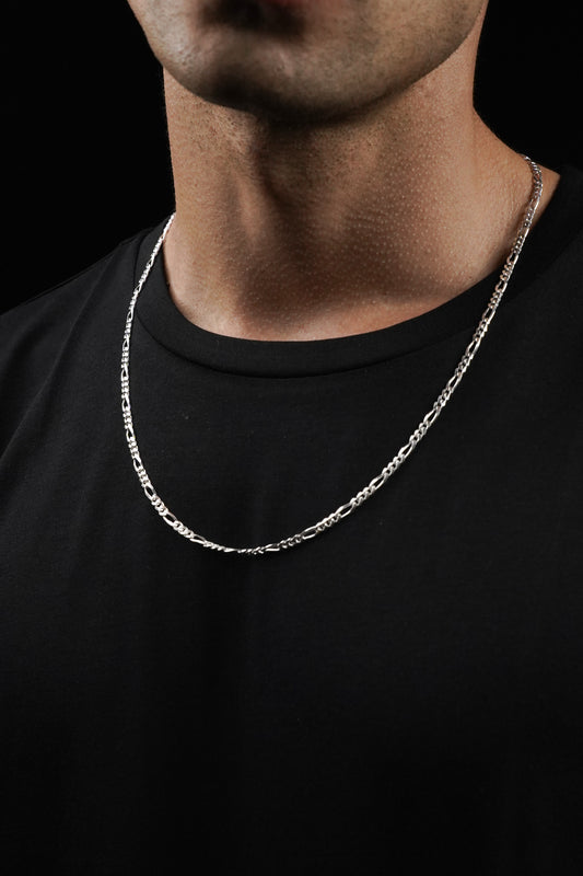 Silver chain necklace on a person wearing a black shirt against a black background