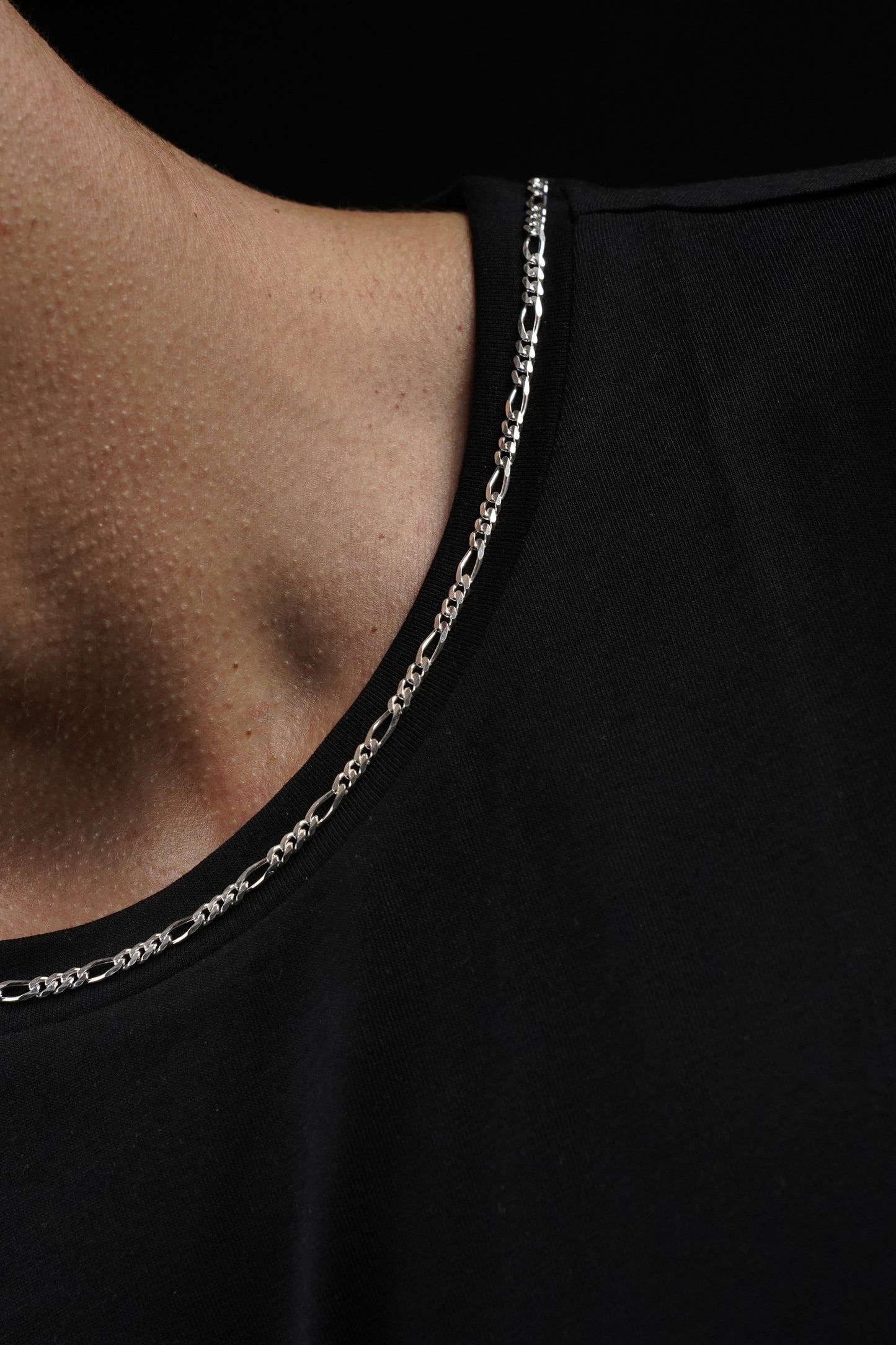 Close-up of a black top with a chain detail on a black background