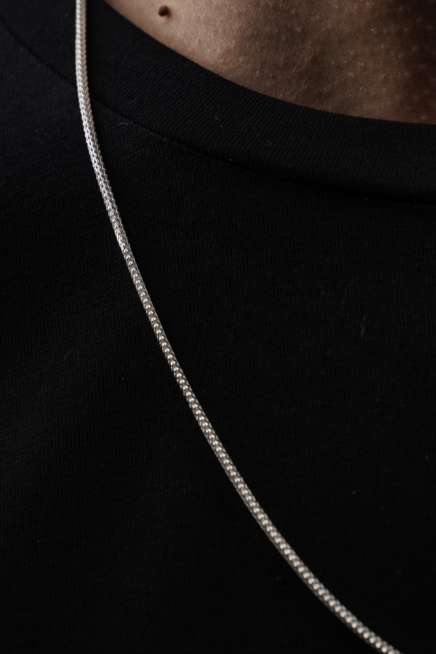Close-up of a silver snake chain necklace on a dark background