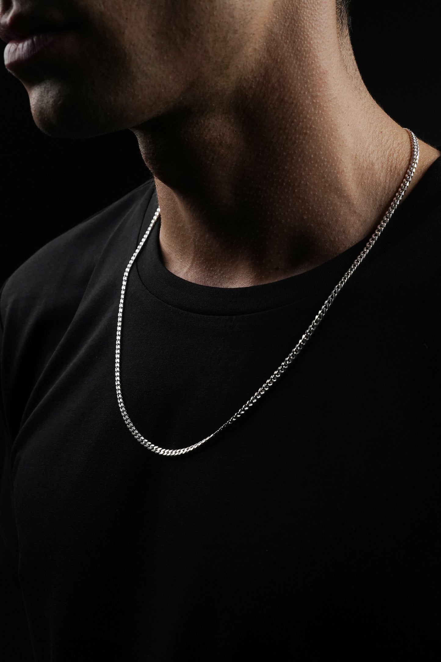 Person wearing a silver chain necklace against a black background