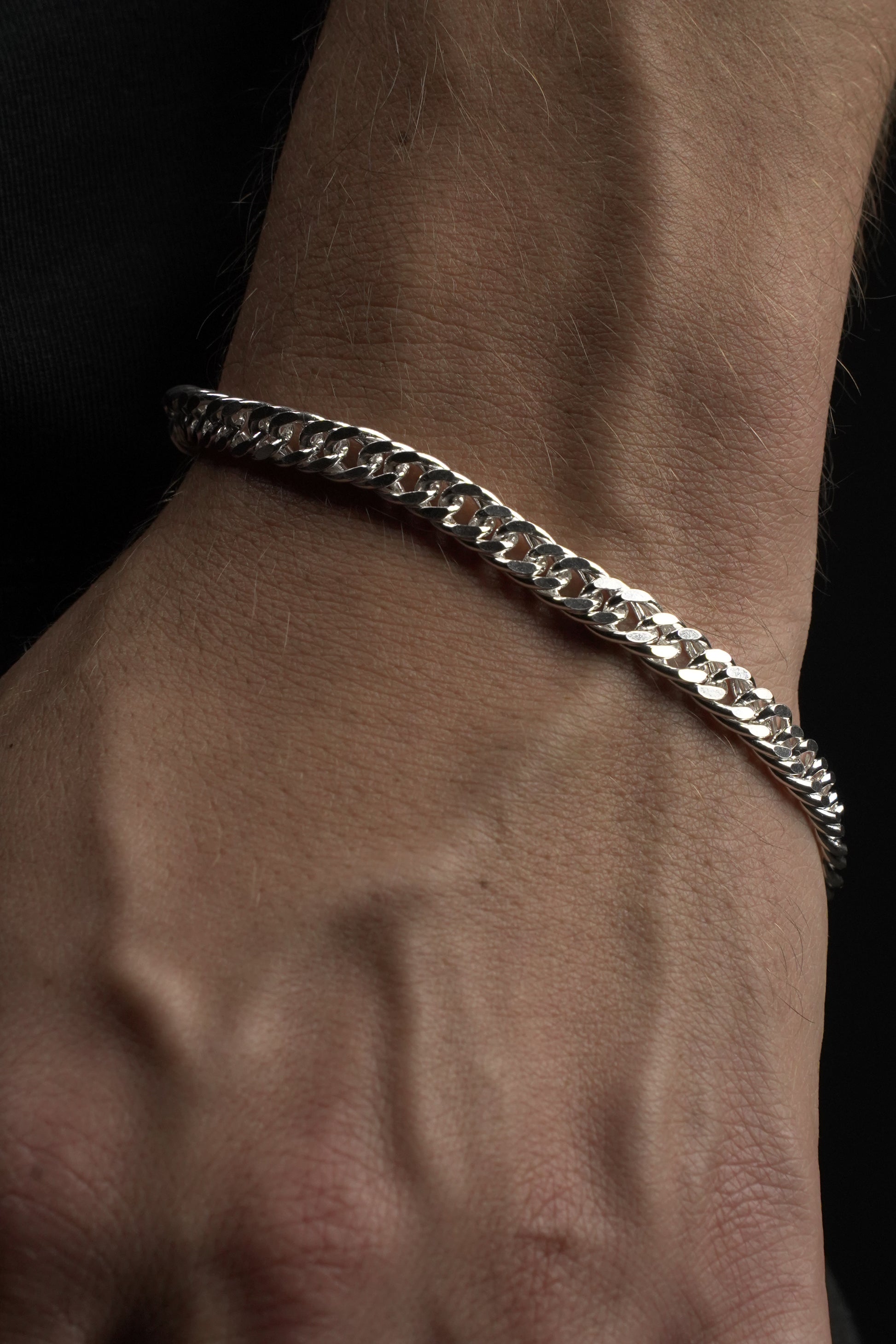 Silver chain bracelet on a wrist against a dark background