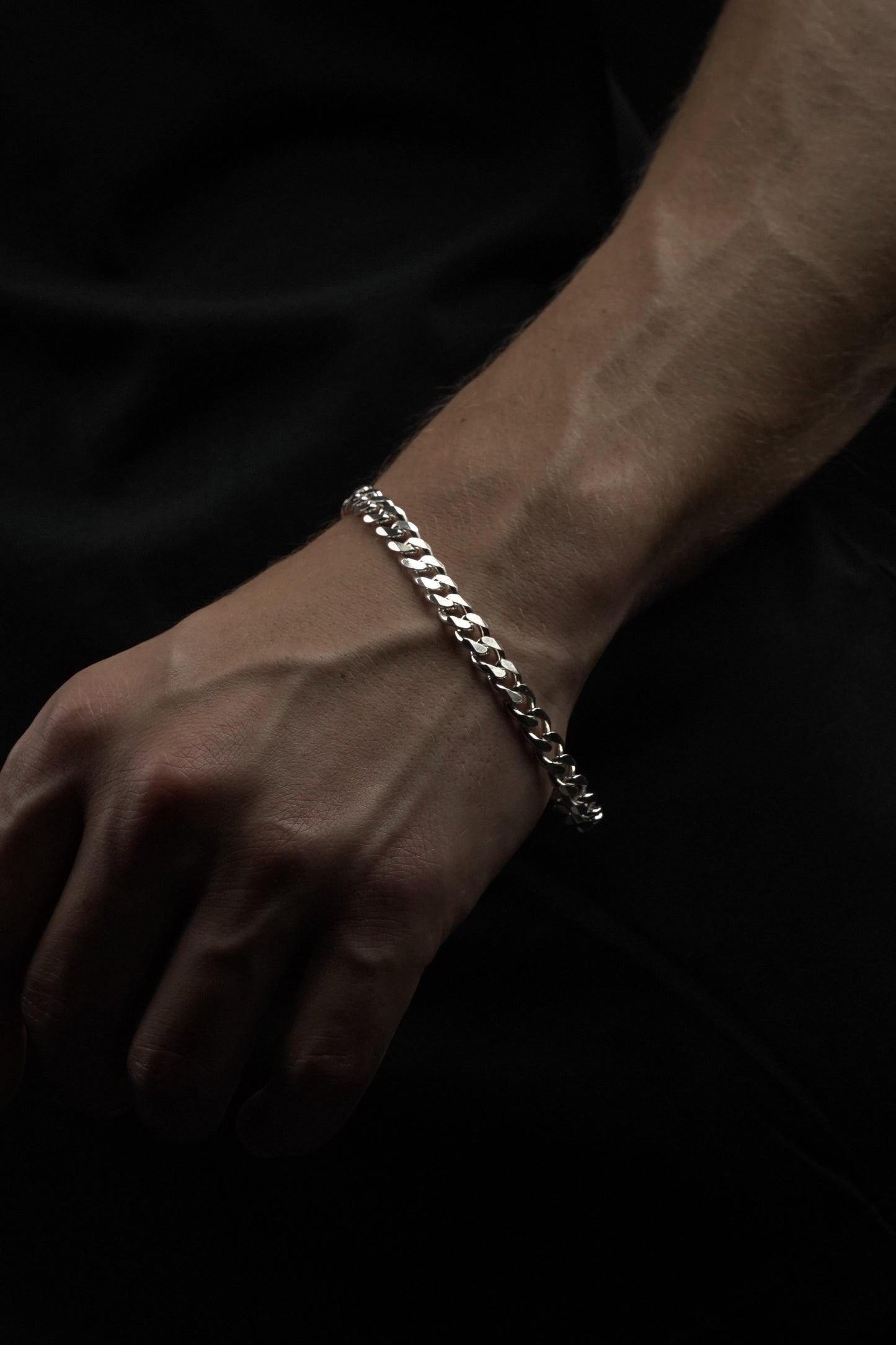Hand wearing a silver chain bracelet on a dark background