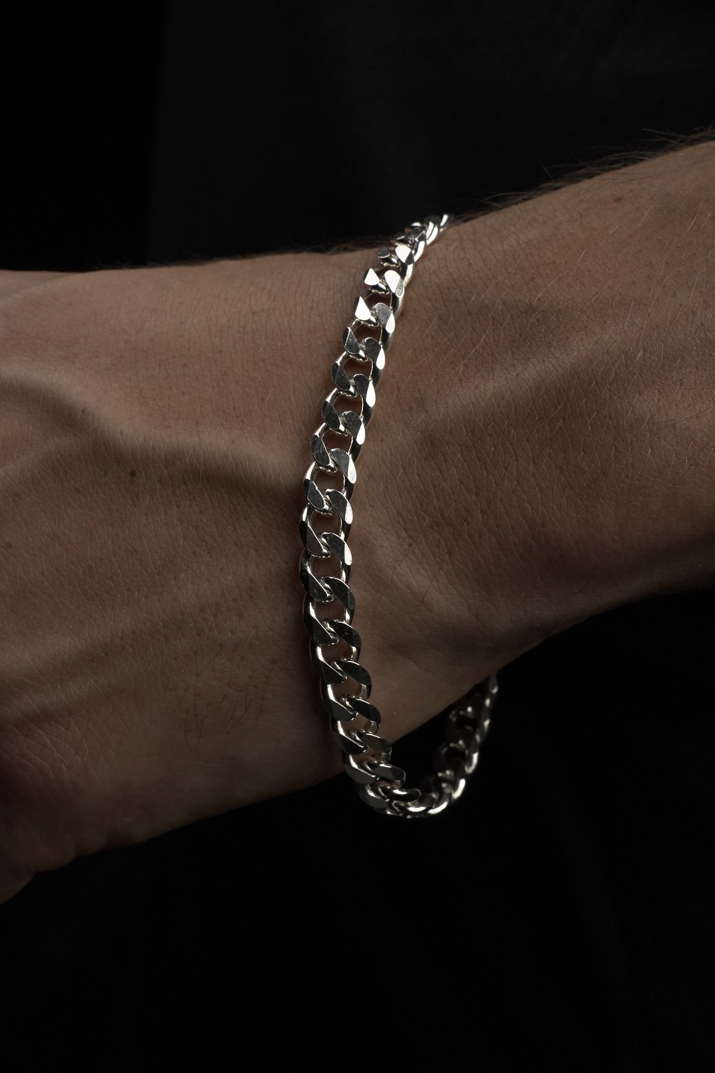 Silver chain bracelet on a wrist against a dark background