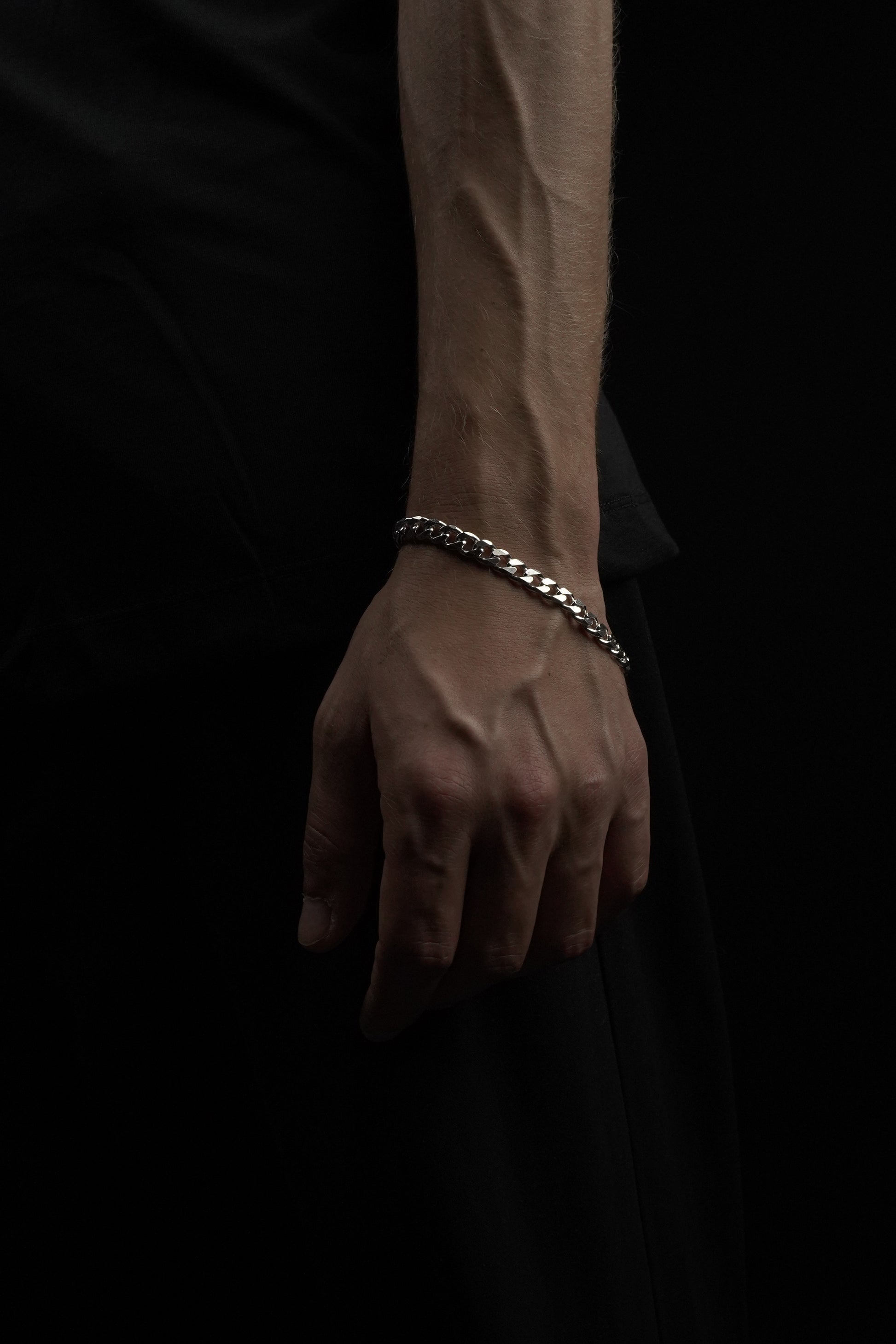 Hand wearing a silver chain bracelet on a dark background