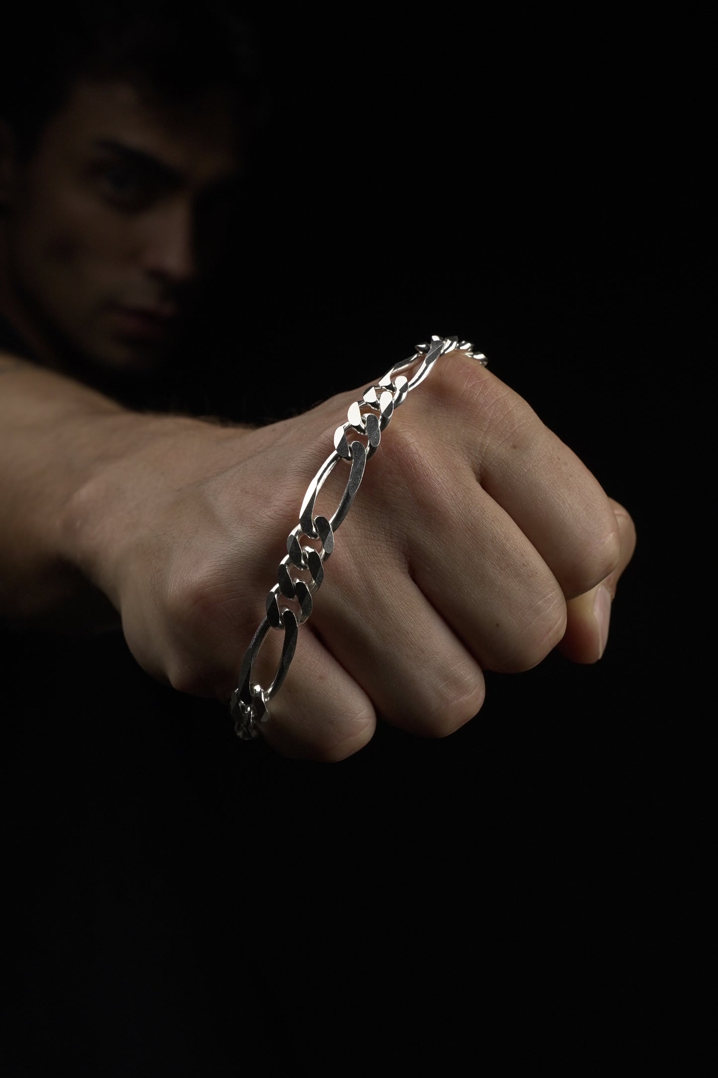 Hand wearing a silver chain bracelet on a dark background