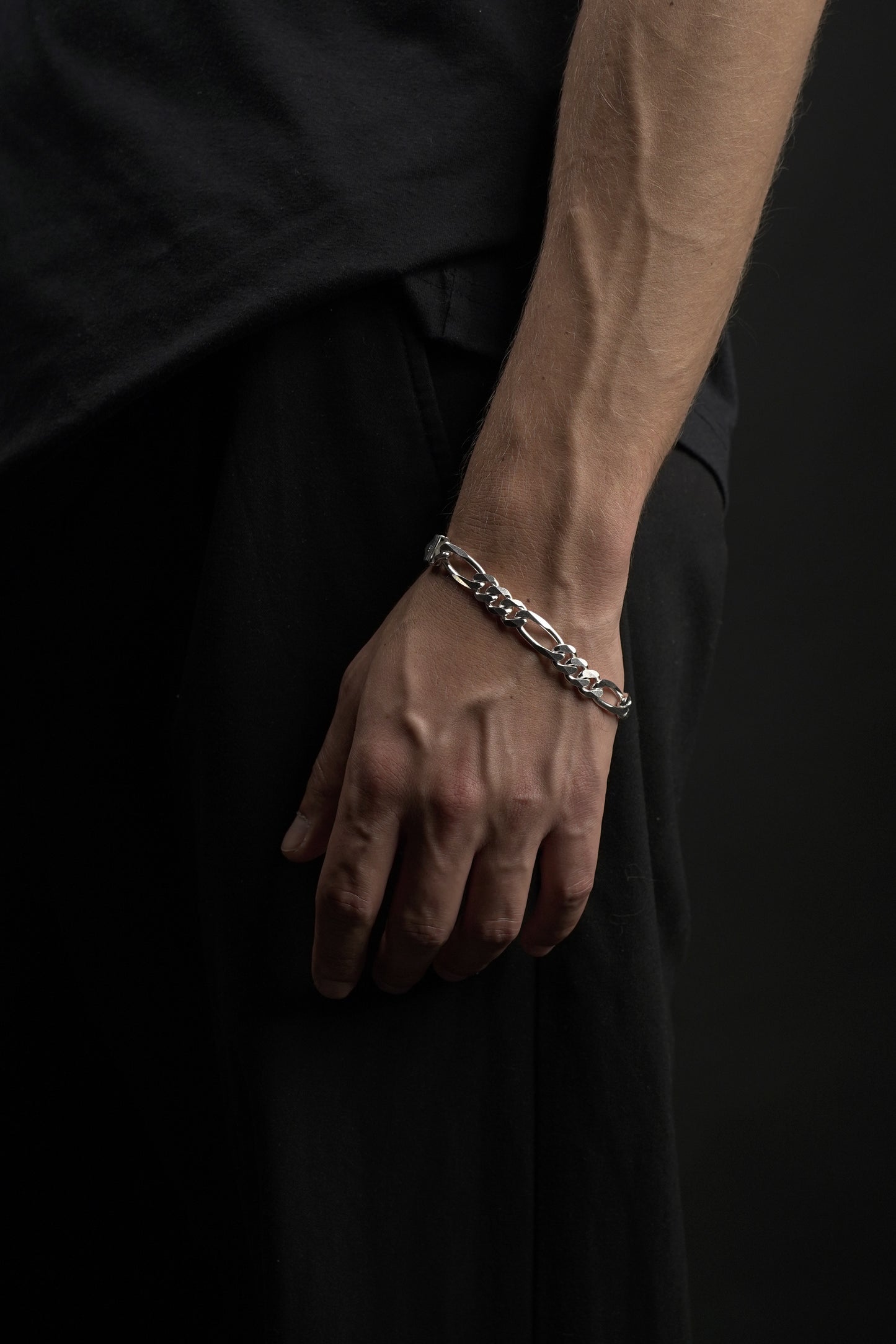 Hand wearing a silver chain bracelet on a dark background