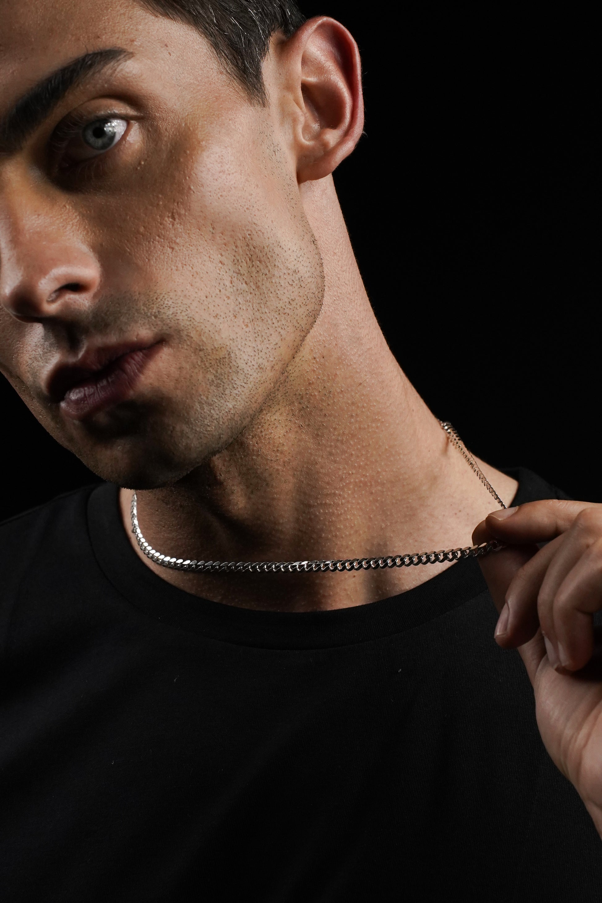 Man wearing a black shirt and chain necklace against a dark background