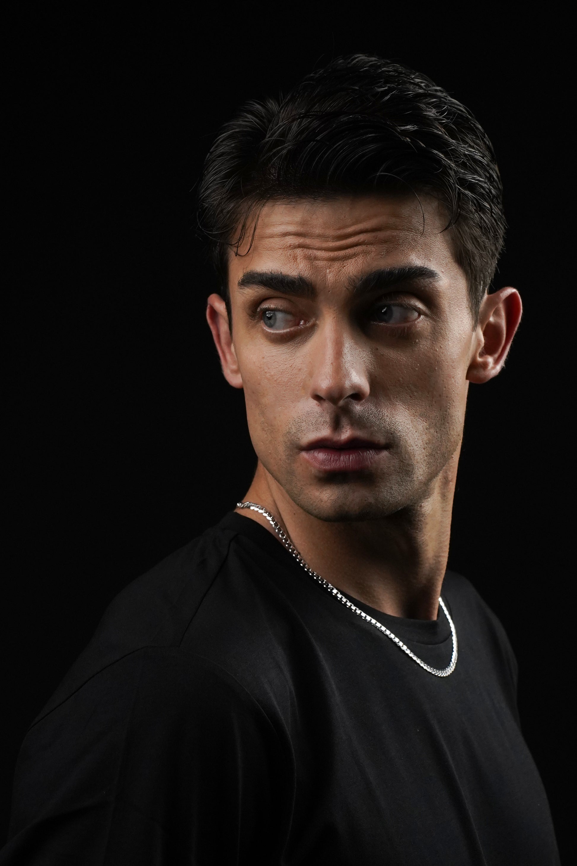 Man wearing a black shirt with a necklace against a dark background