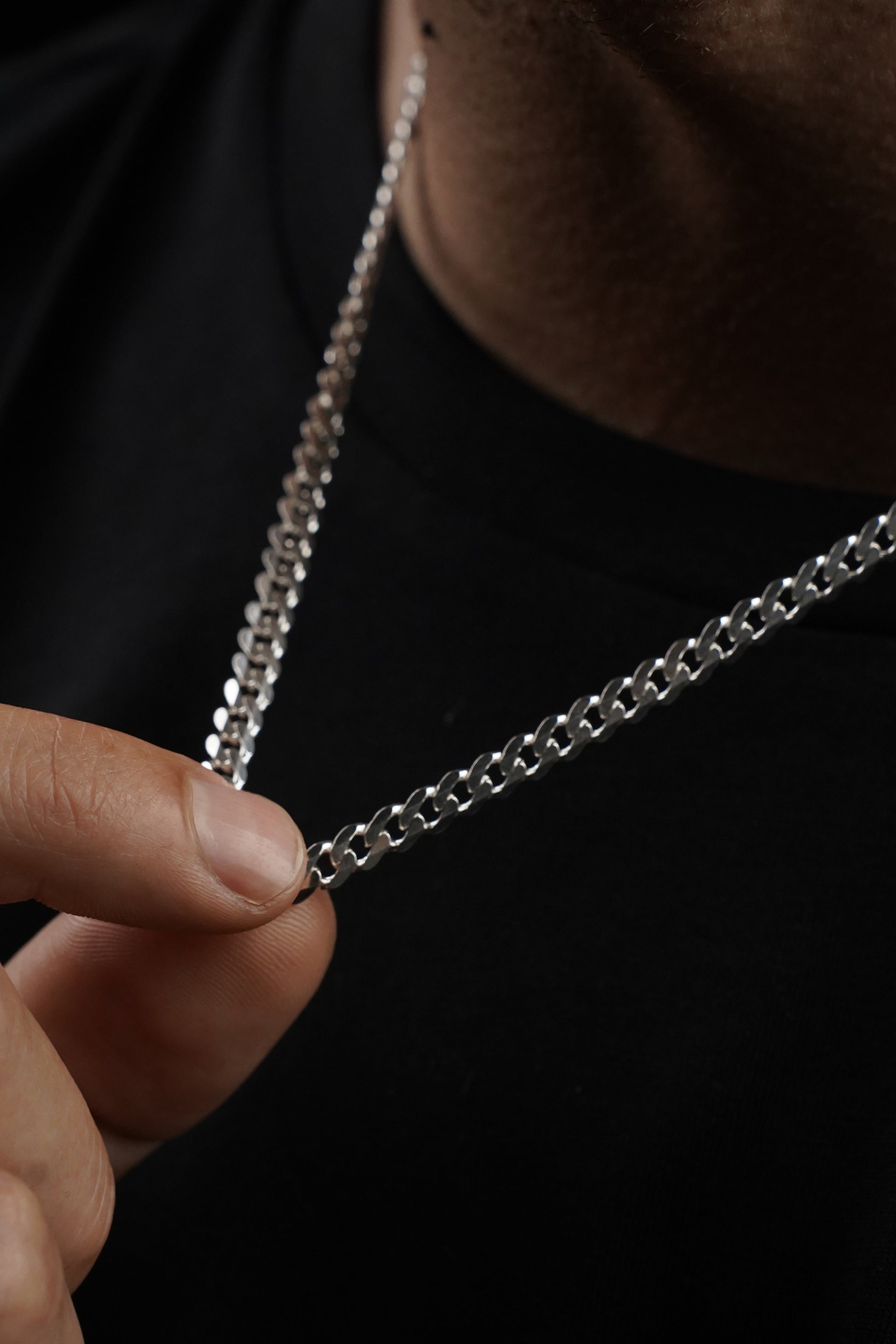 Close-up of a silver chain held by a hand against a dark background