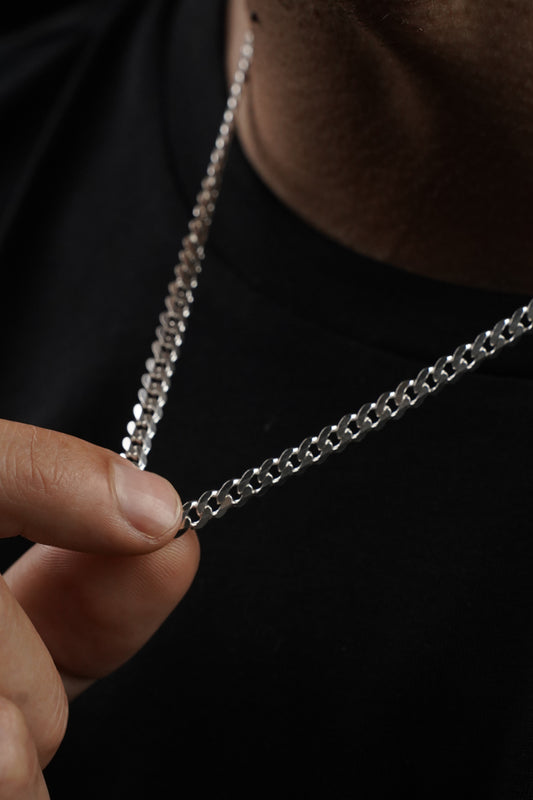 Close-up of a silver chain held by a hand against a dark background