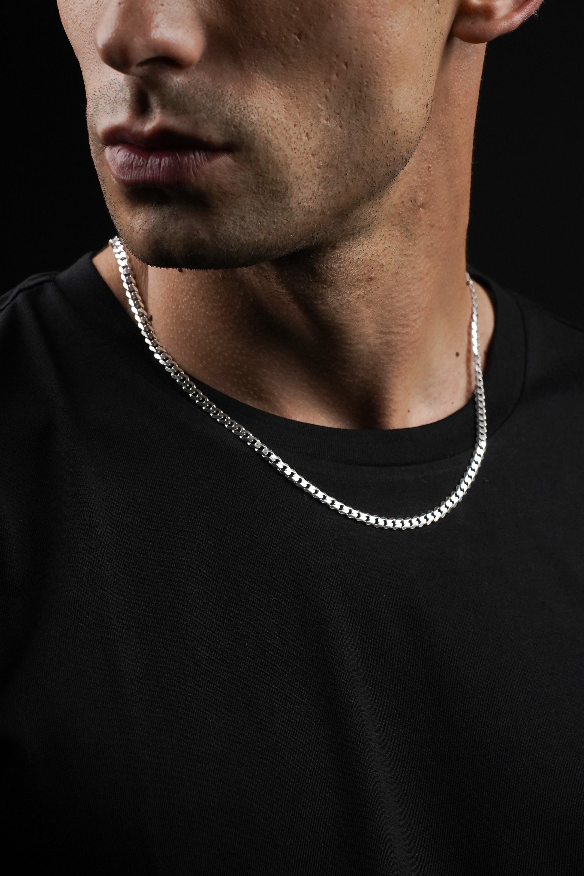 Man wearing a silver chain necklace against a black background