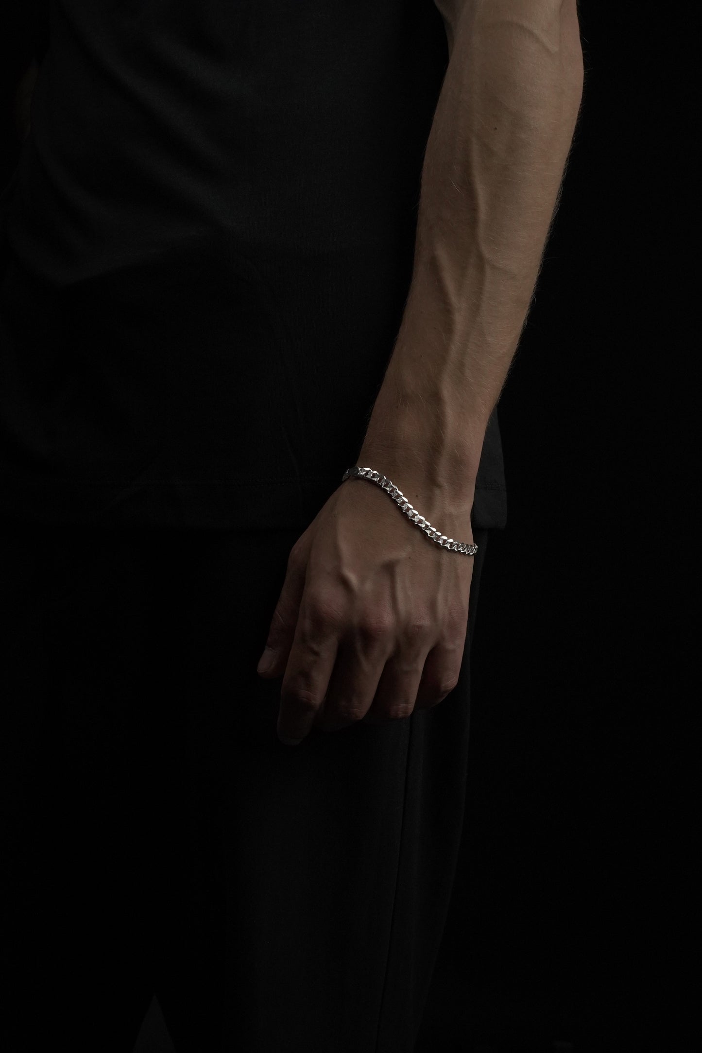 Hand wearing a silver bracelet on a dark background