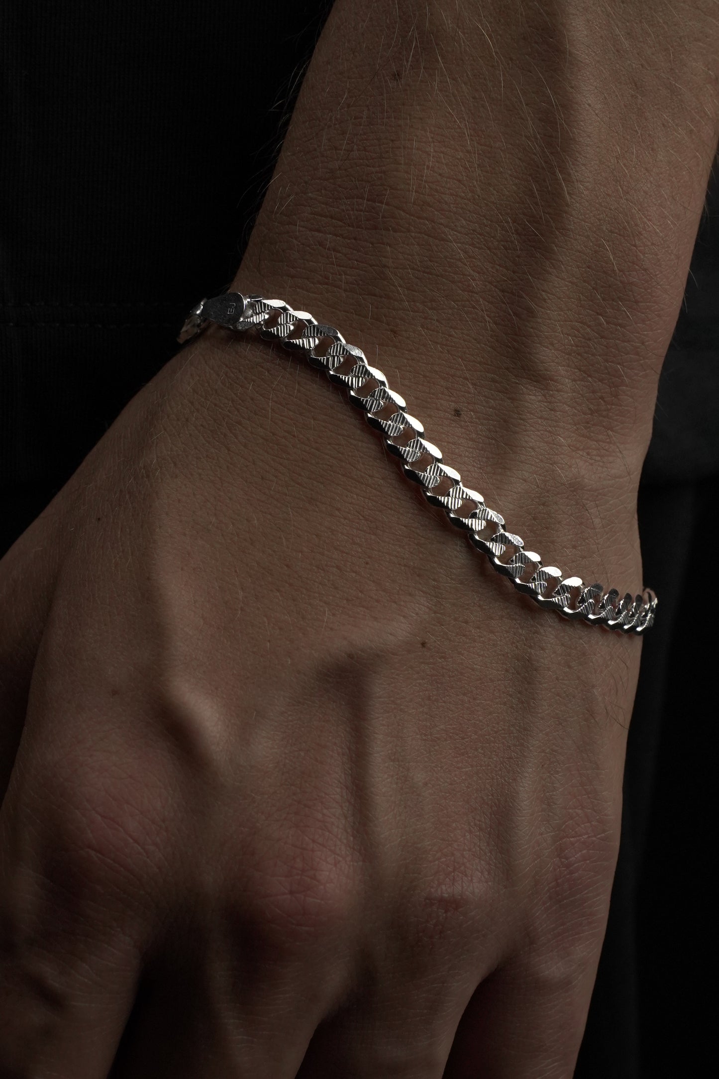 Silver chain bracelet on a wrist against a dark background