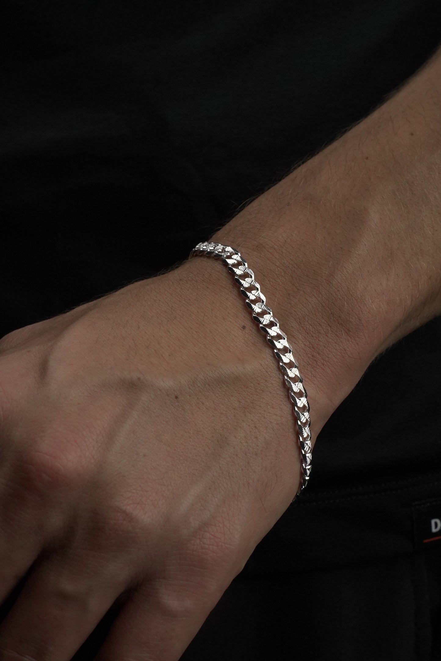 Silver bracelet on a wrist against a dark background