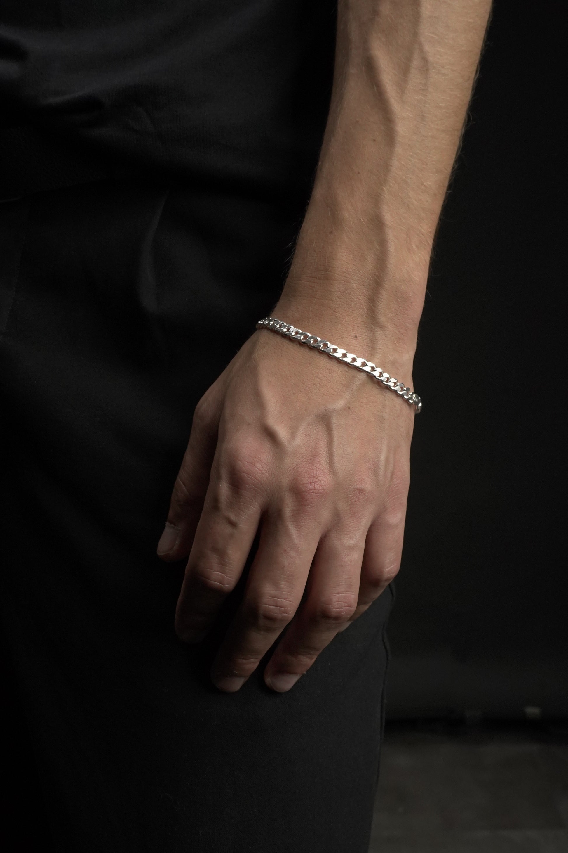 Hand wearing a silver bracelet on a dark background