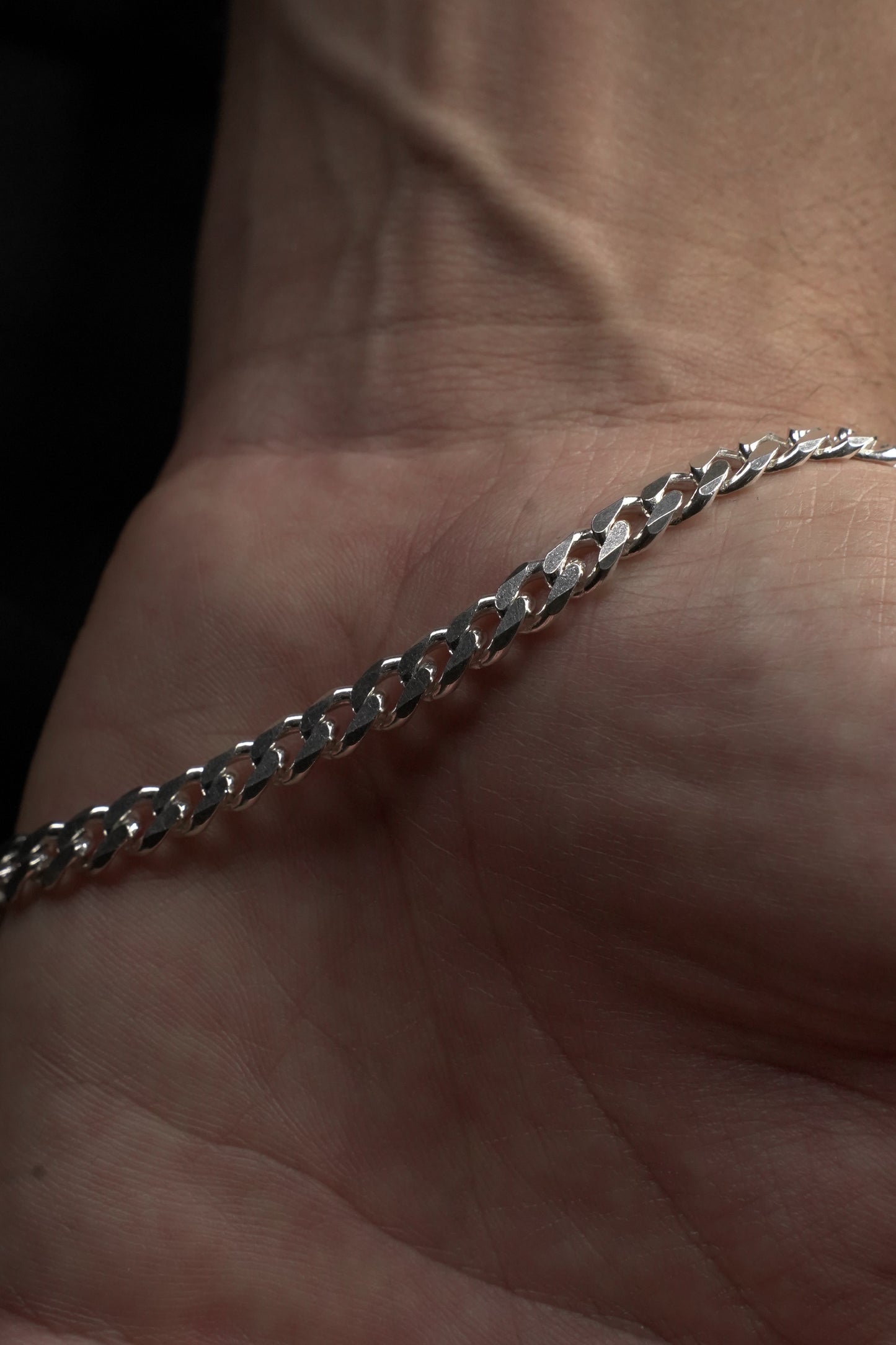 Silver chain held between fingers against a dark background