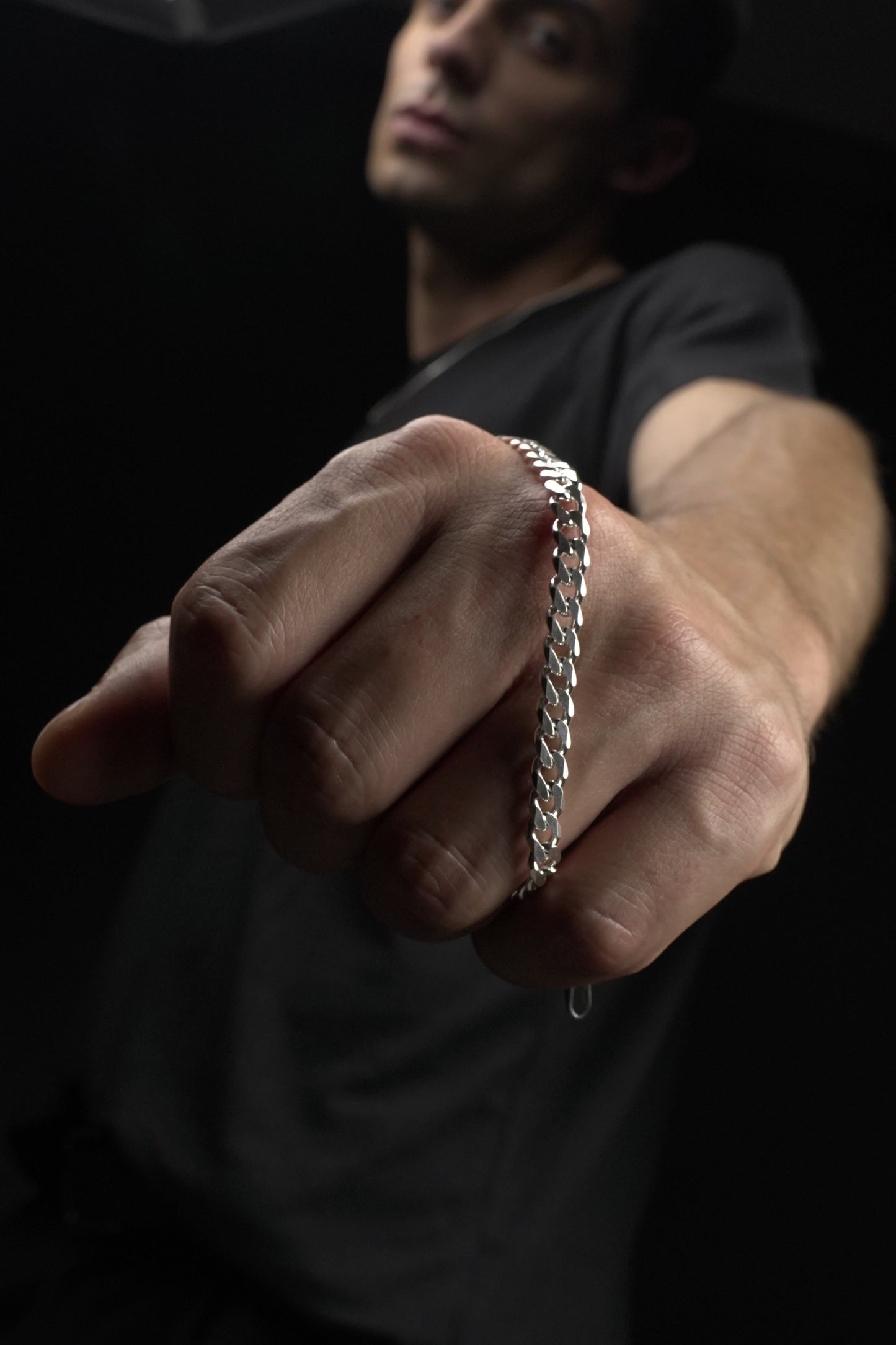 Hand wearing a silver bracelet on a dark background
