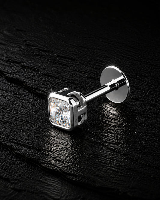 A single silver stud earring with a square-cut clear gemstone, displayed on a textured black background.