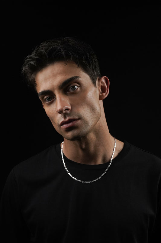 Man wearing a black shirt and silver necklace against a black background