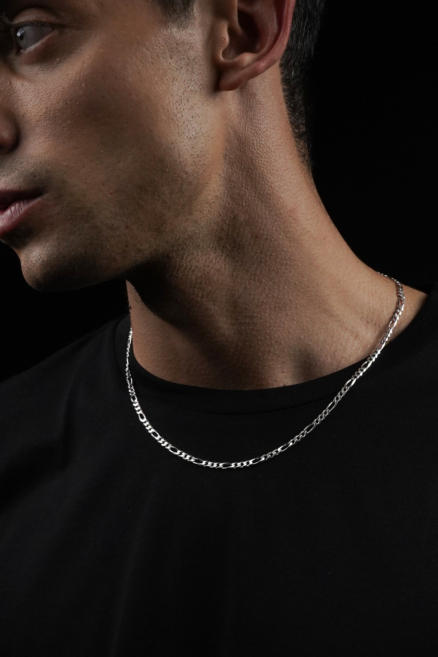 Close-up of a person wearing a silver chain necklace against a black background