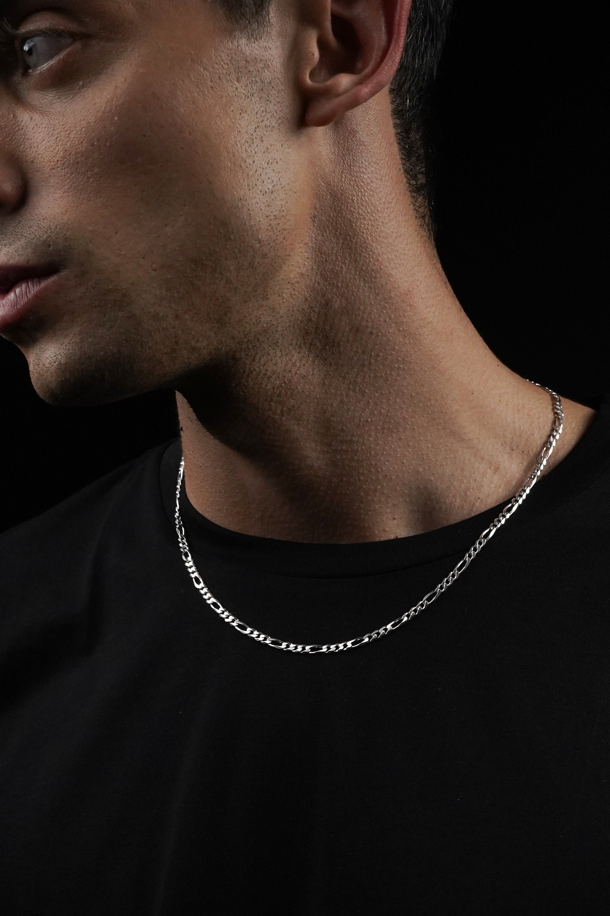 Close-up of a person wearing a silver chain necklace against a black background