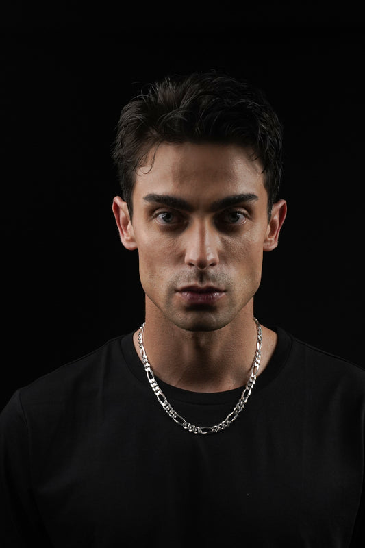 Man wearing a black shirt and silver chain necklace against a black background