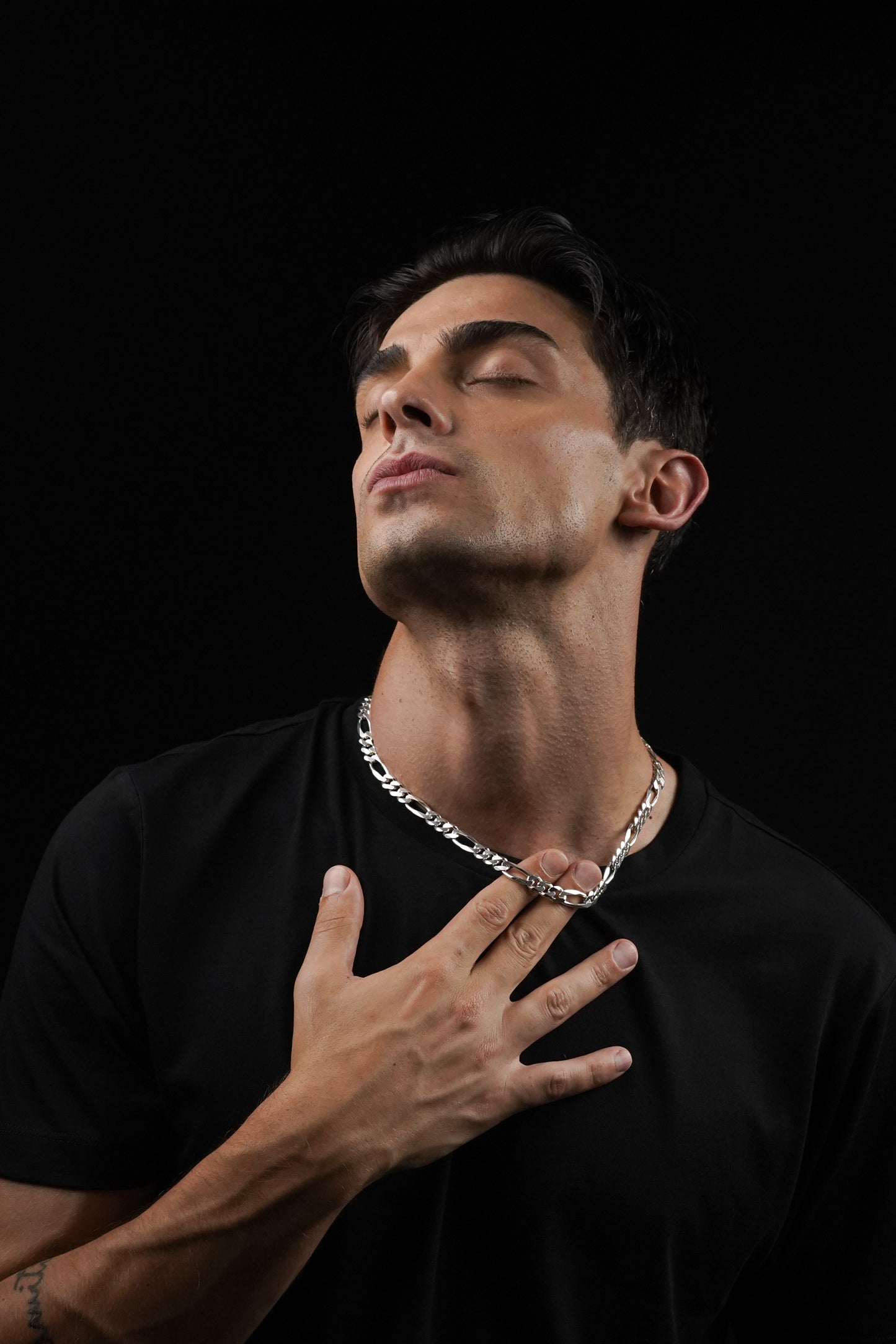 Man wearing a black shirt and silver chain necklace against a black background