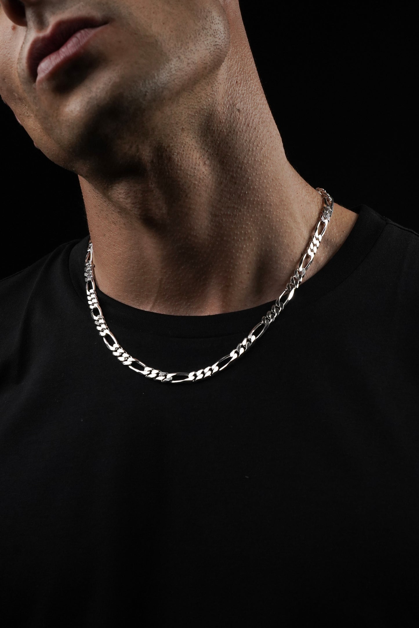 Man wearing a silver chain necklace against a black background
