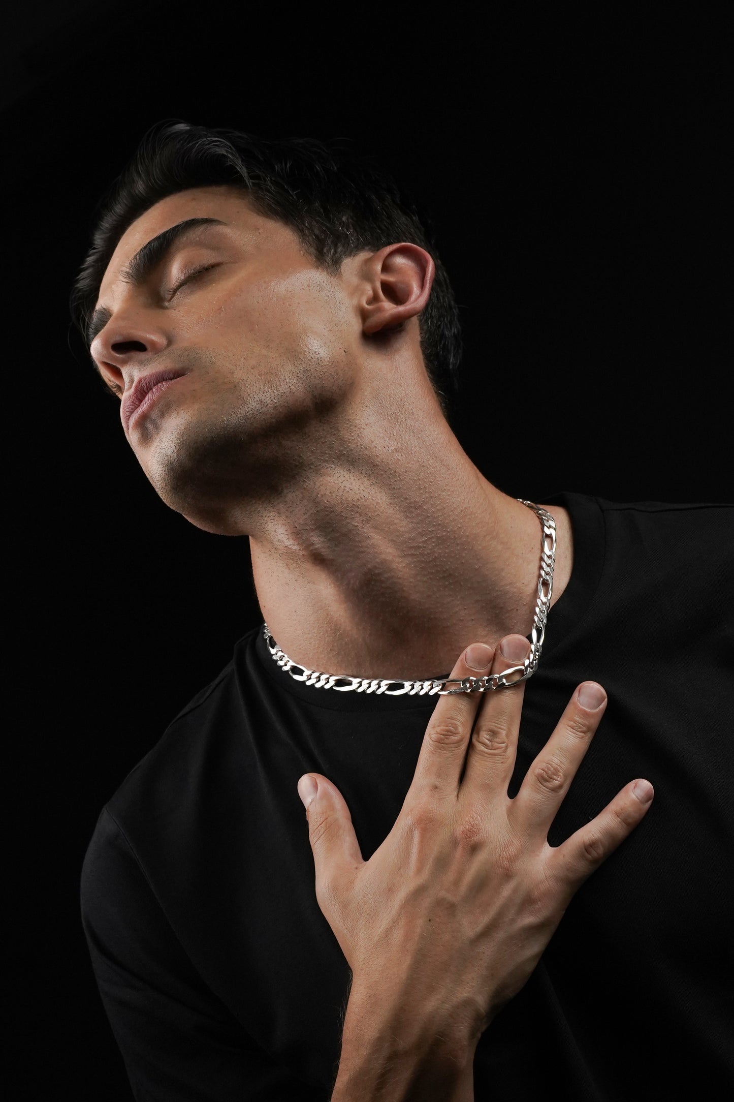 Man wearing a silver chain necklace against a black background