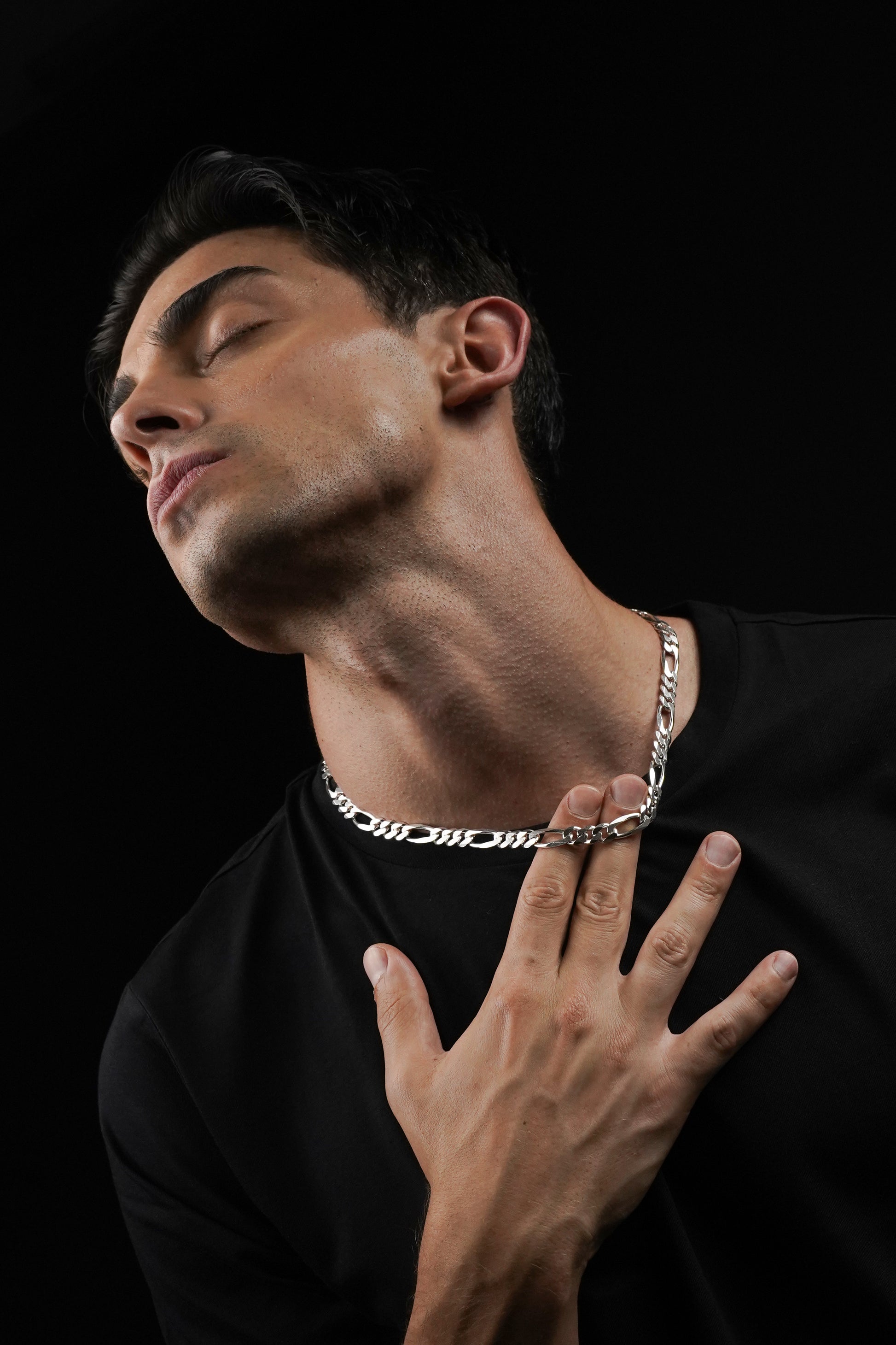 Man wearing a silver chain necklace against a black background