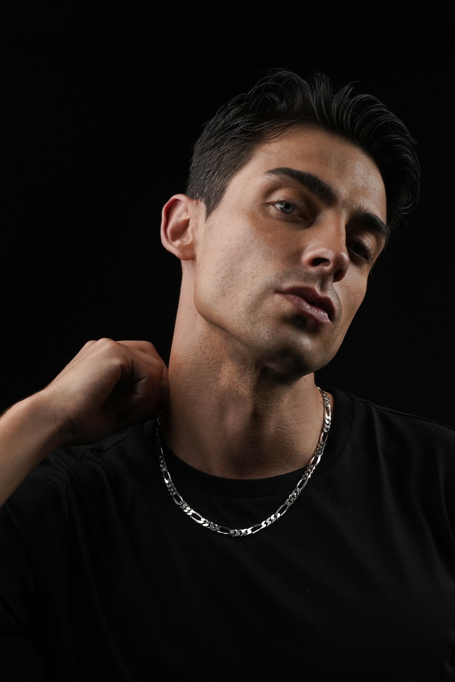 Man wearing a black shirt and silver chain necklace against a black background