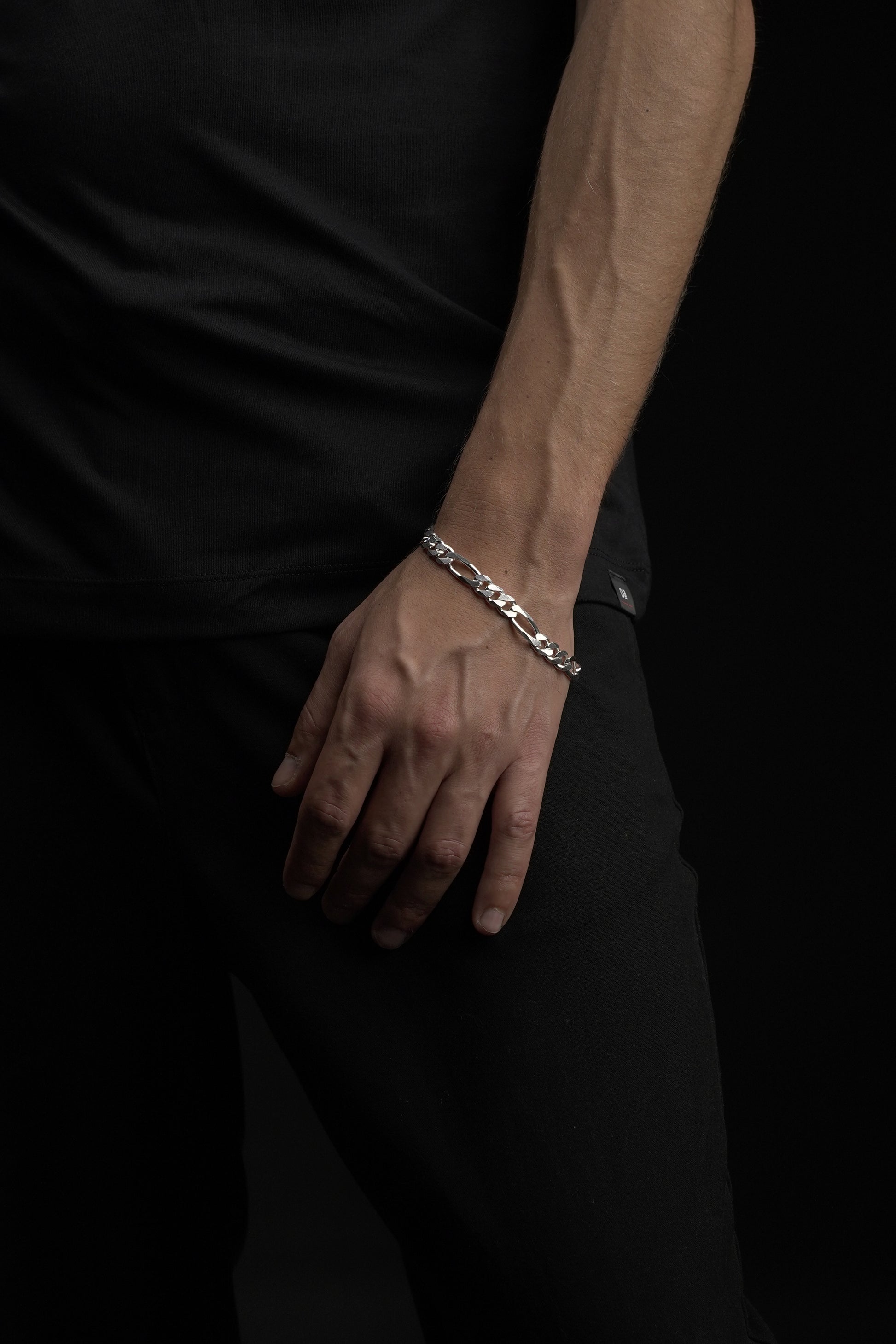 Hand wearing a silver bracelet on a dark background