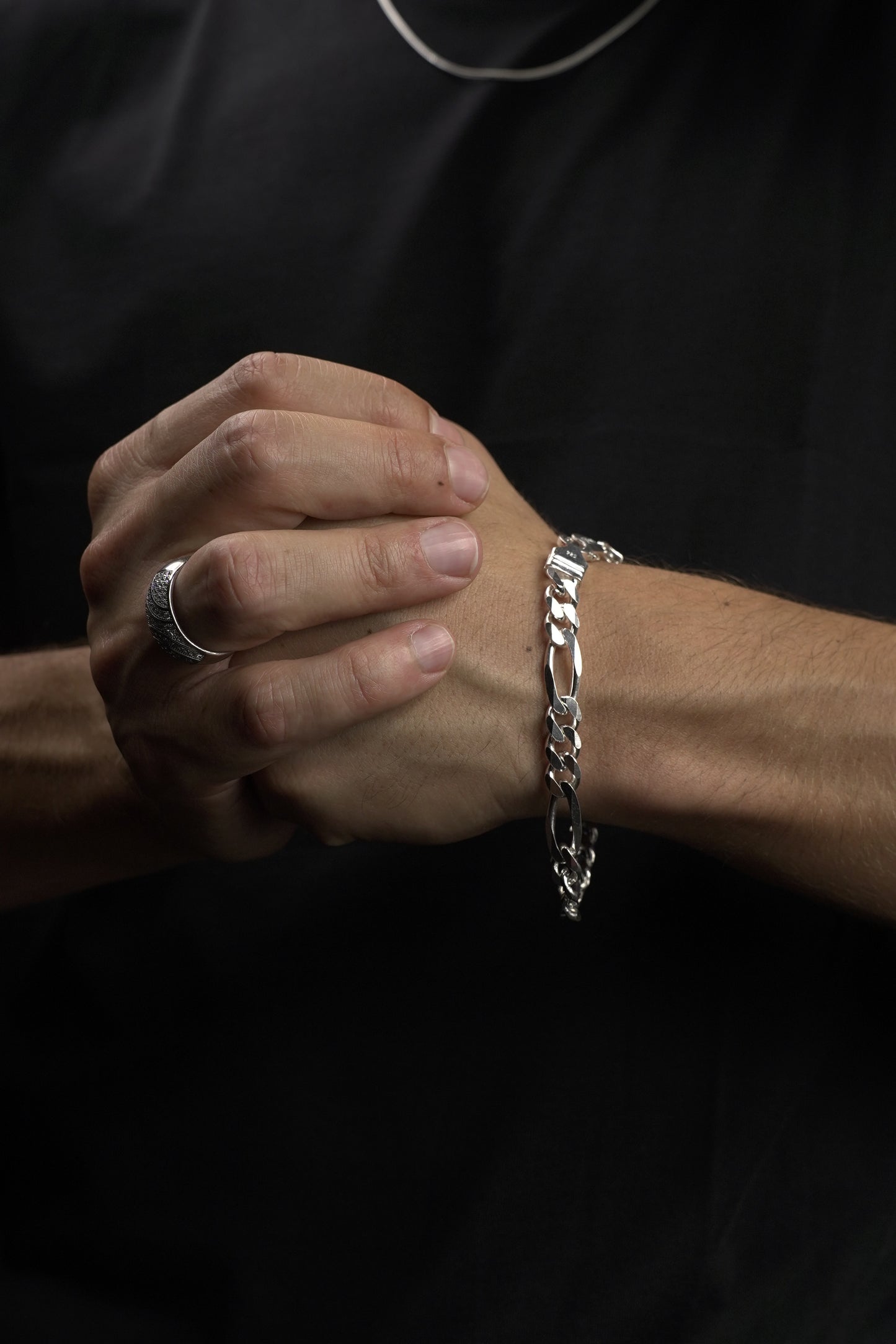 Close-up of a hand wearing a silver bracelet on a dark background