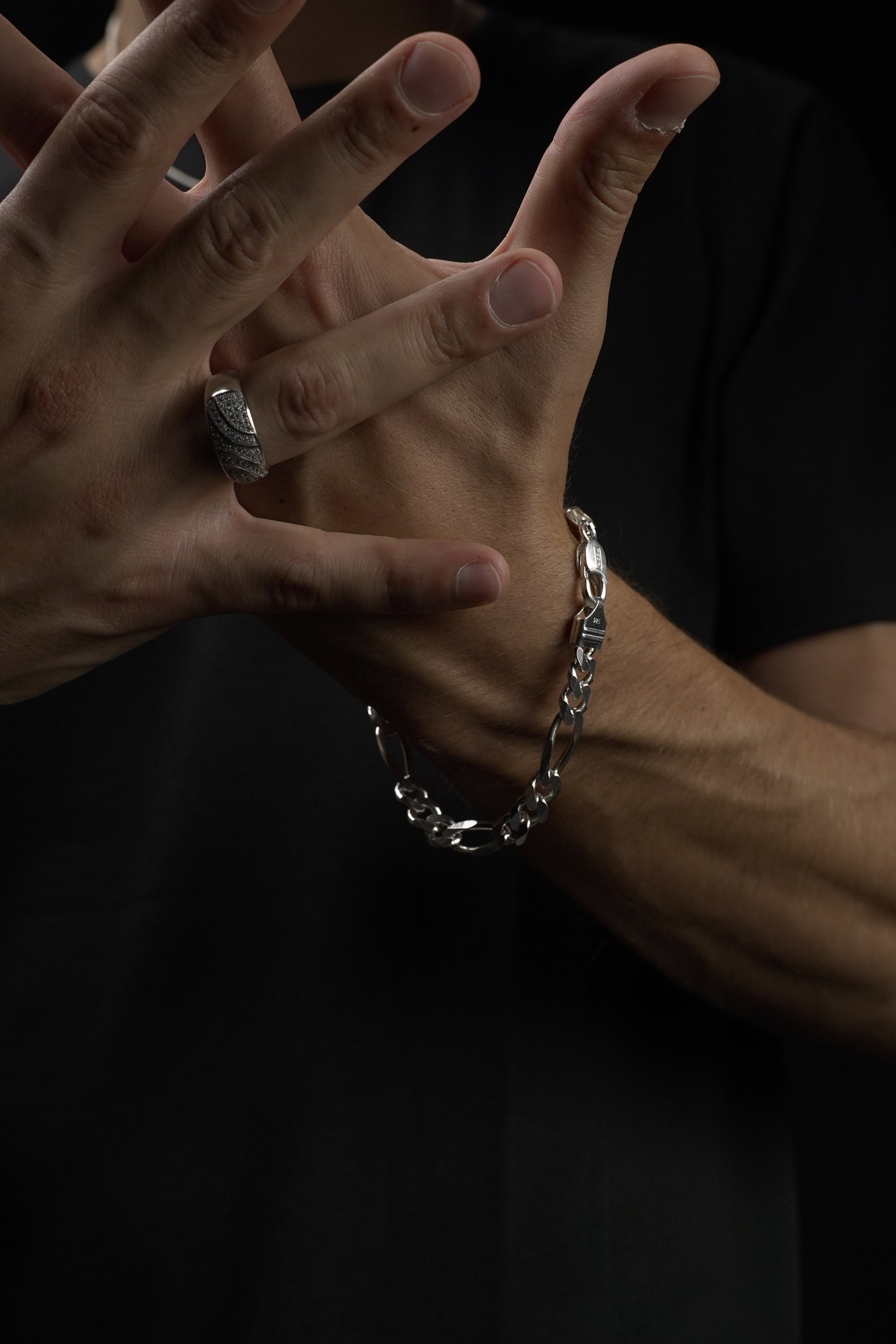 Close-up of hands with a bracelet and ring on a dark background