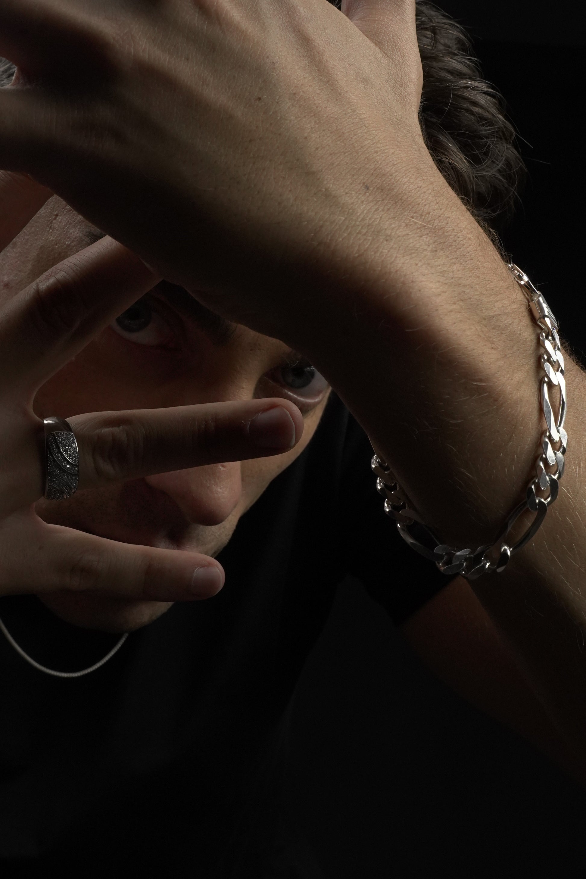 Close-up of a person's arm with a silver chain bracelet and a ring on a dark background