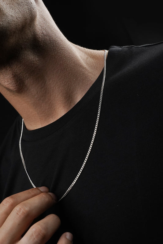 Silver chain necklace worn by a person against a black background
