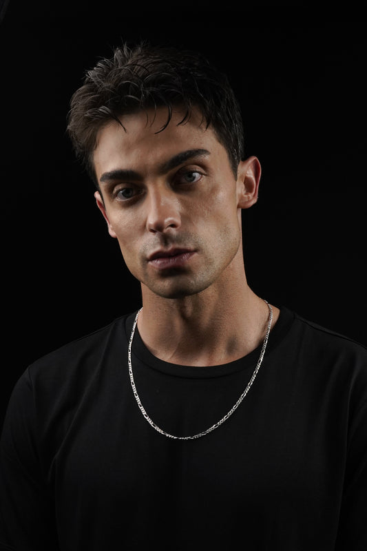 Man wearing a black shirt and silver chain necklace against a black background