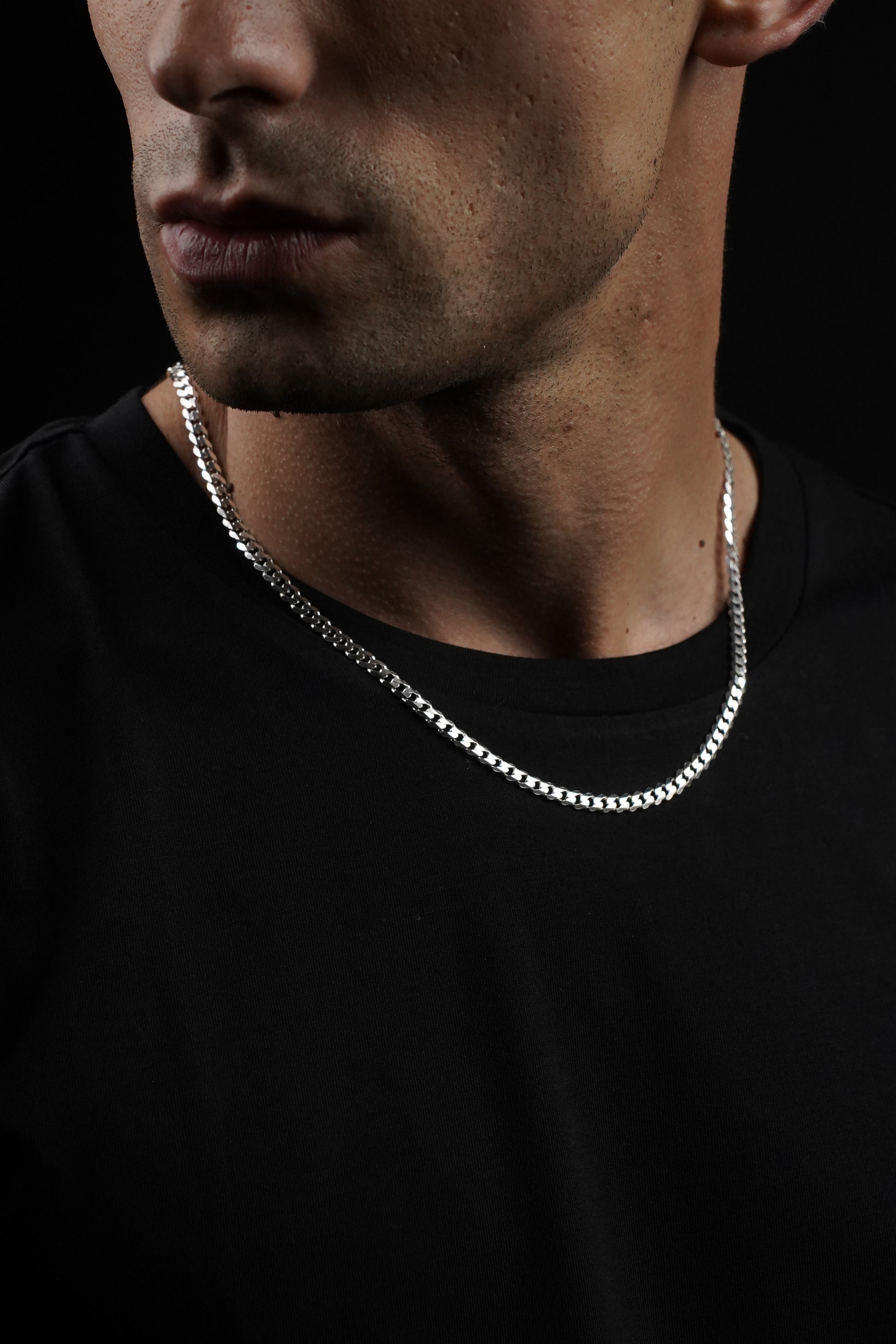 Close-up of a person wearing a silver chain necklace against a black background