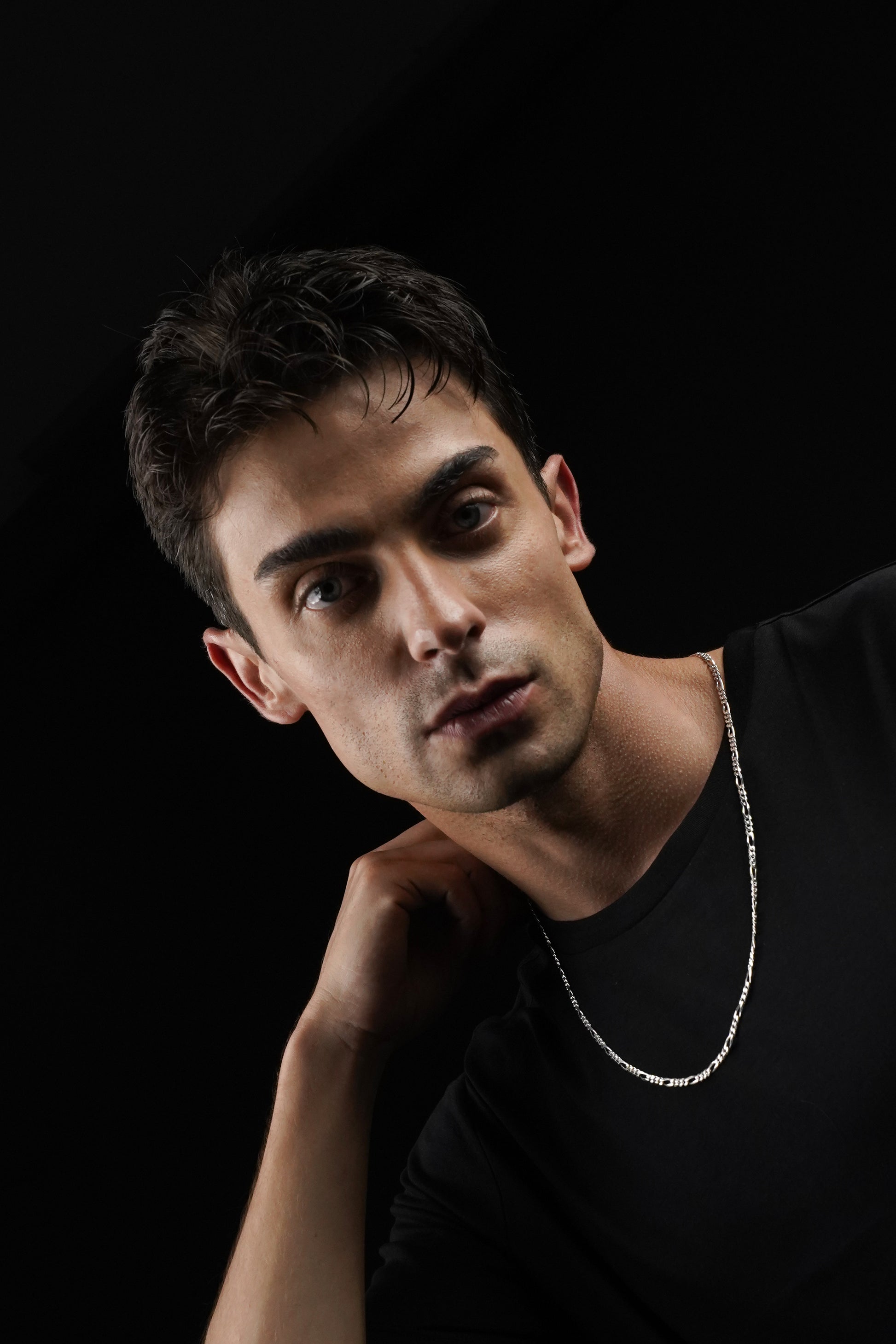 Man wearing a black shirt and silver necklace against a dark background
