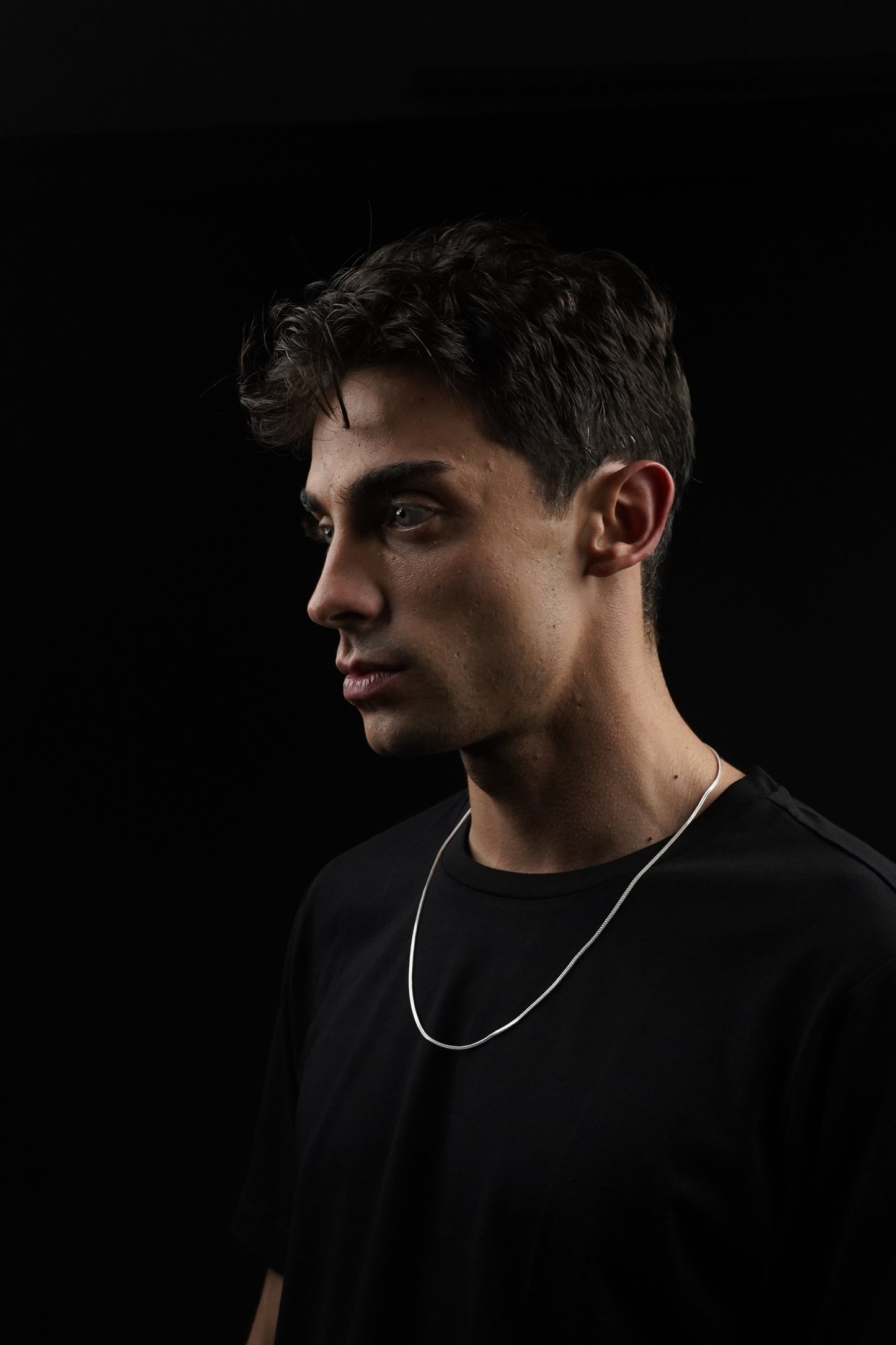 Man wearing a black shirt with white earphones on a dark background