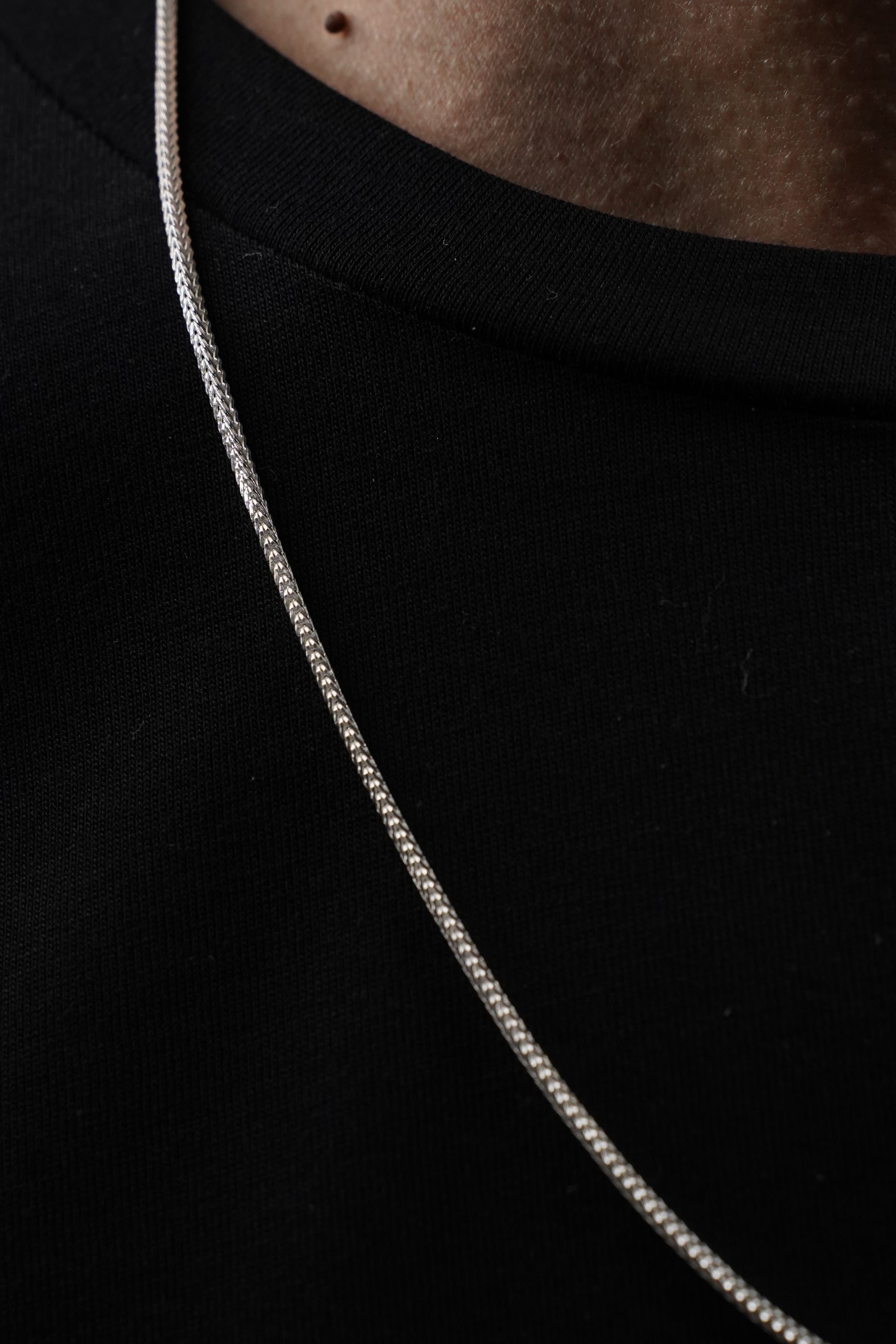 Close-up of a silver snake chain necklace on a dark background