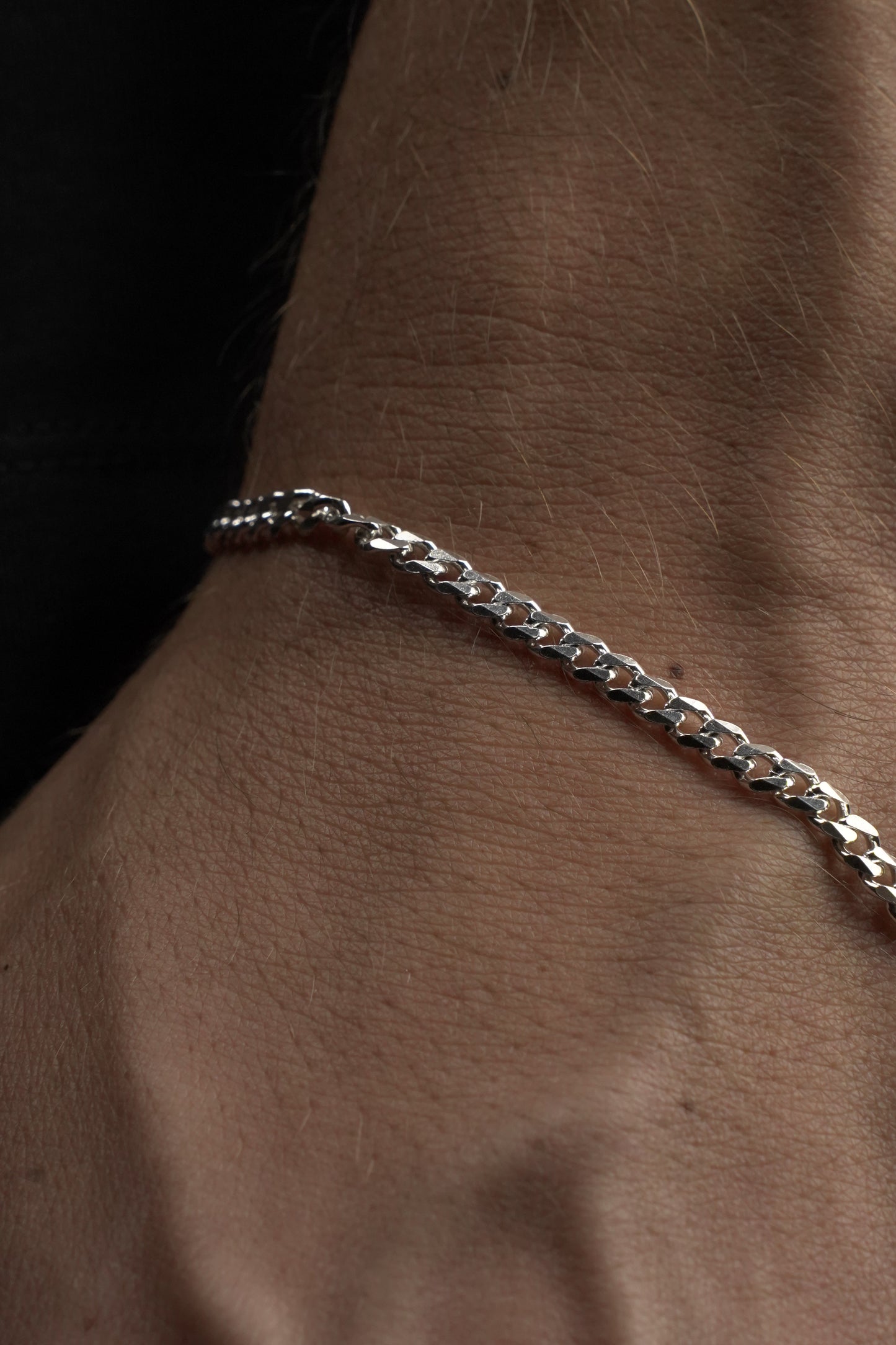 Silver chain bracelet on a wrist against a dark background