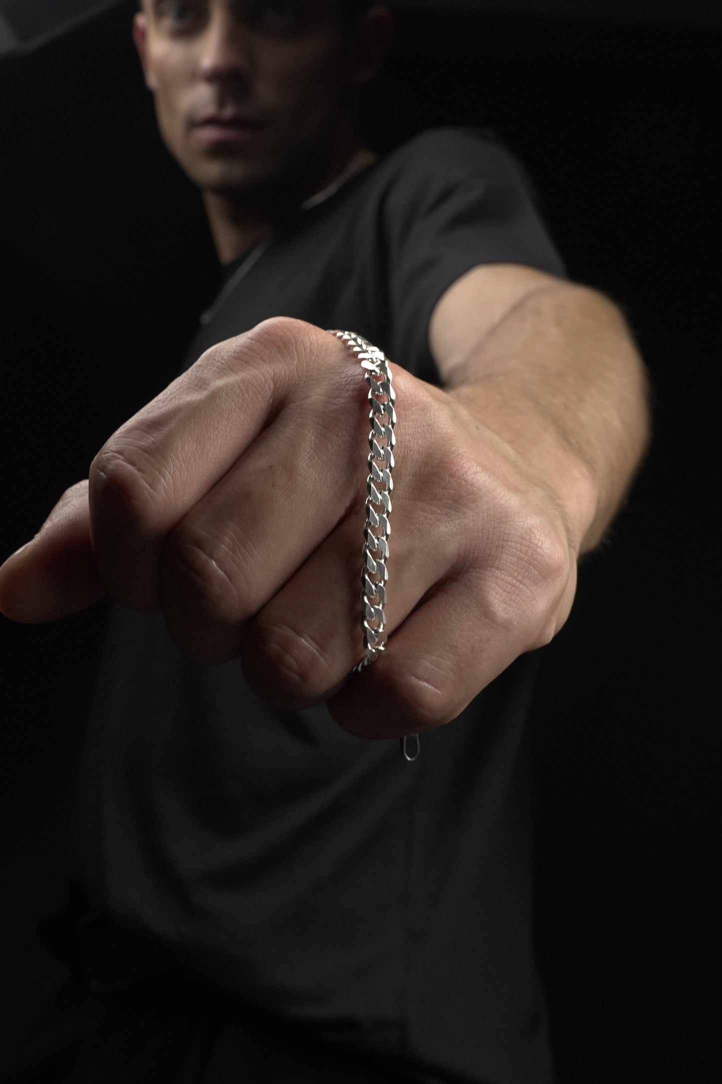 Hand wearing a silver bracelet against a dark background