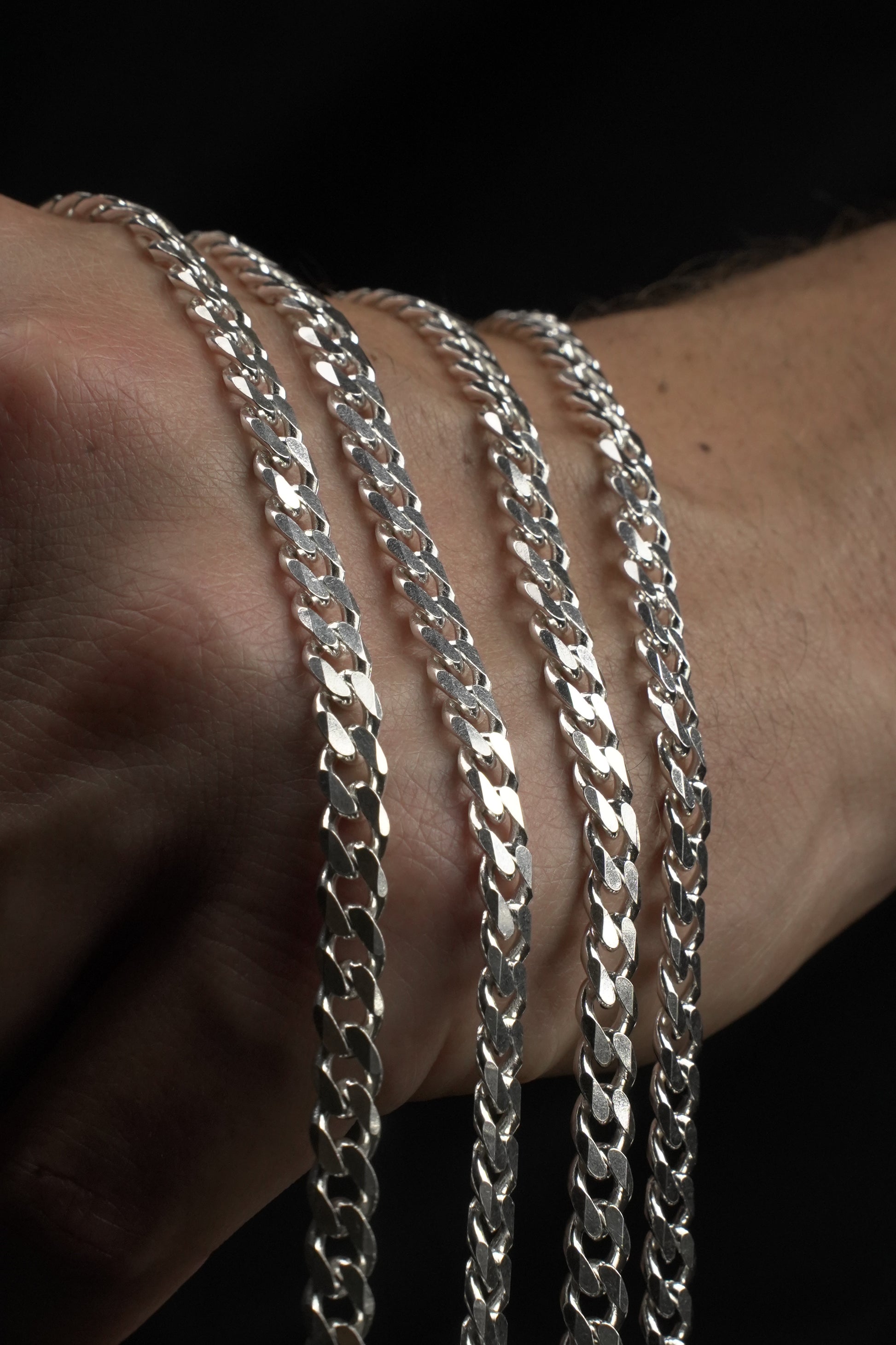 Silver chain bracelets on a wrist against a dark background
