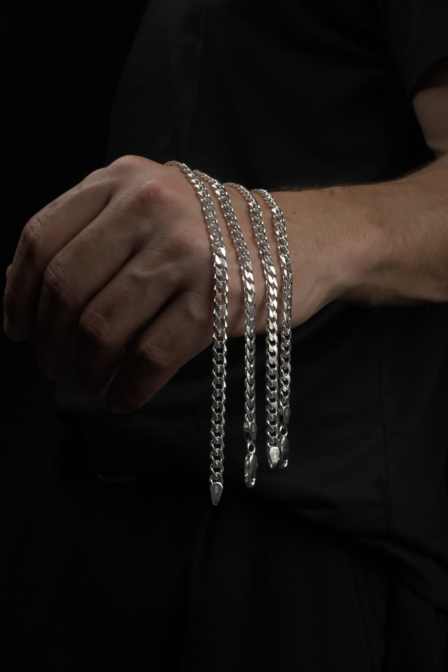 Hand wearing multiple silver bracelets on a dark background