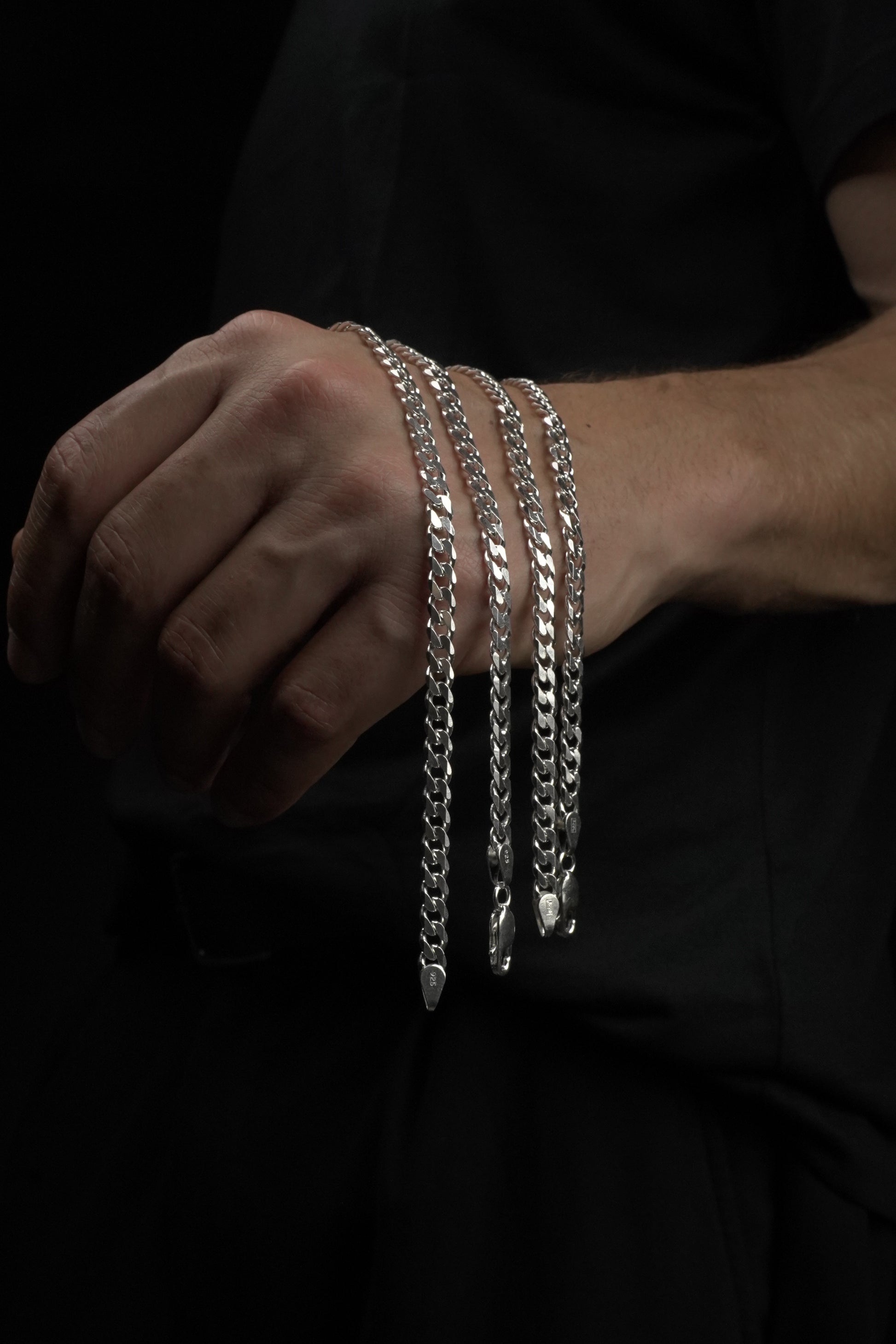 Hand wearing multiple silver bracelets on a dark background