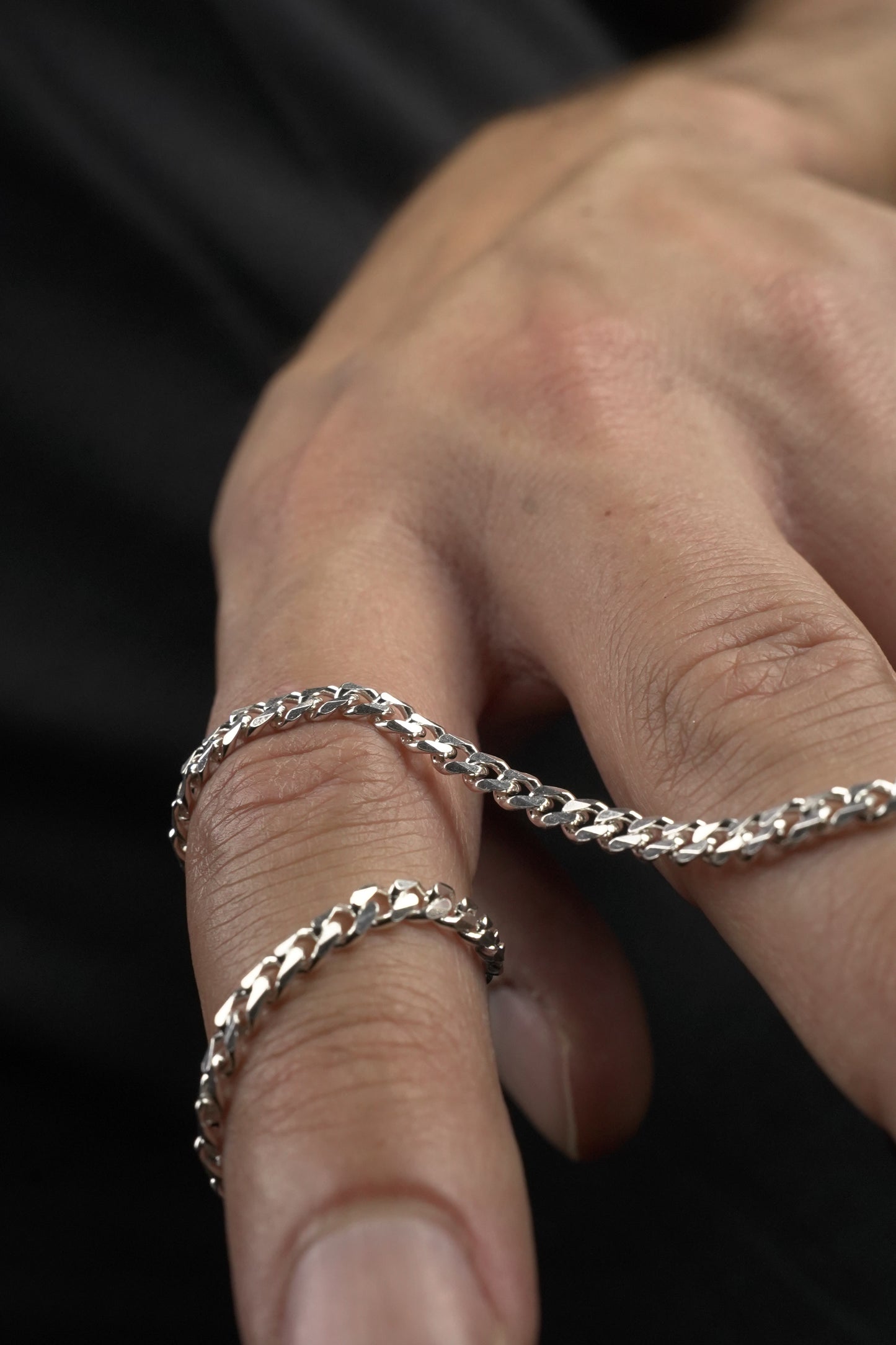 Close-up of a hand wearing a silver chain bracelet against a dark background